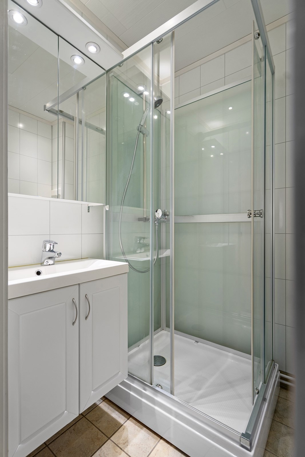 Badet inneholder servant med underskap, speilskap med lys og oppbevaring, dusjkabinett, toalett og opplegg for vaskemaskin Galleribilde