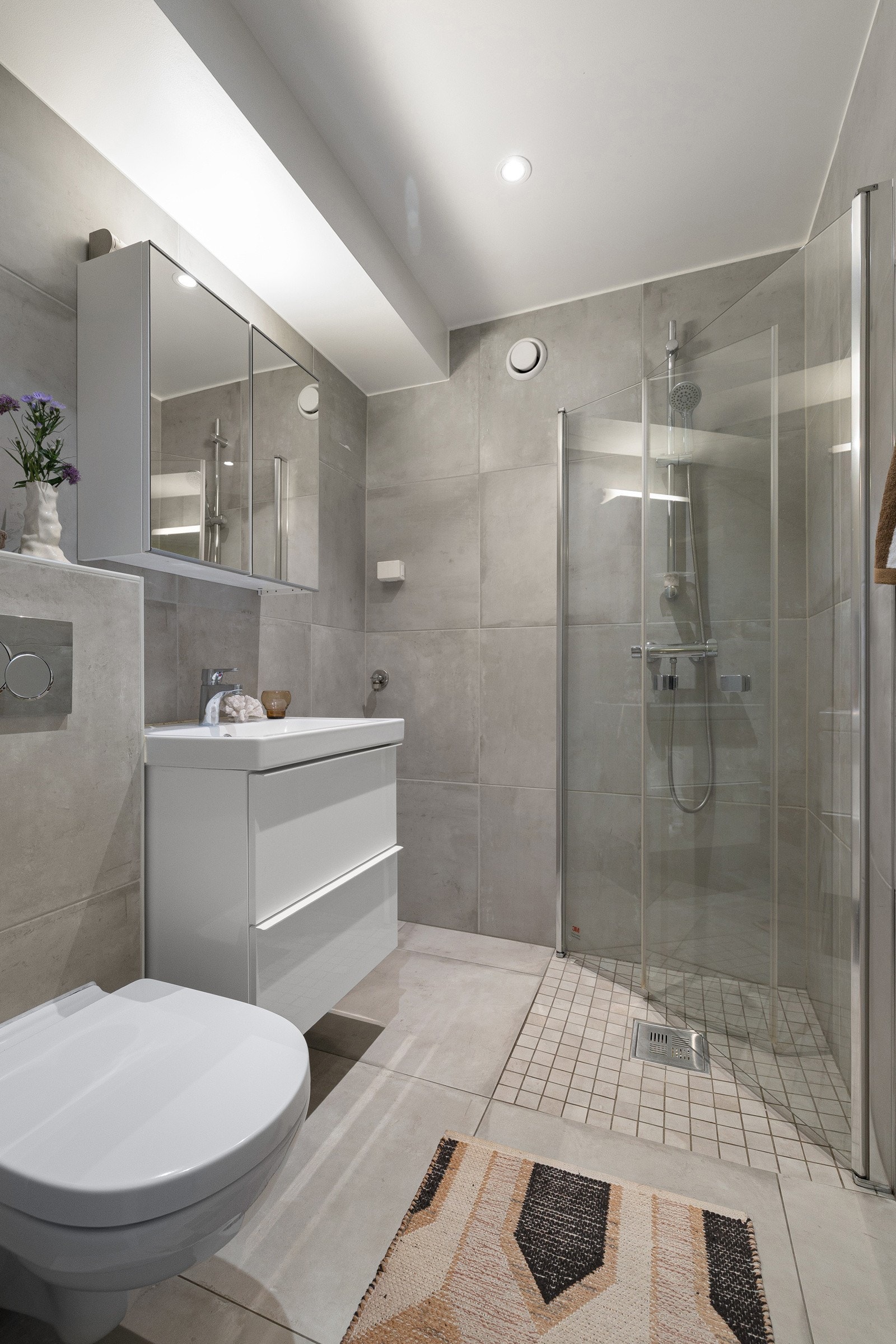 Innredning med servant og gode oppbevaringsmuligheter, vegghengt toalett samt dusjhjørne med innfellbare glassdører. Galleribilde