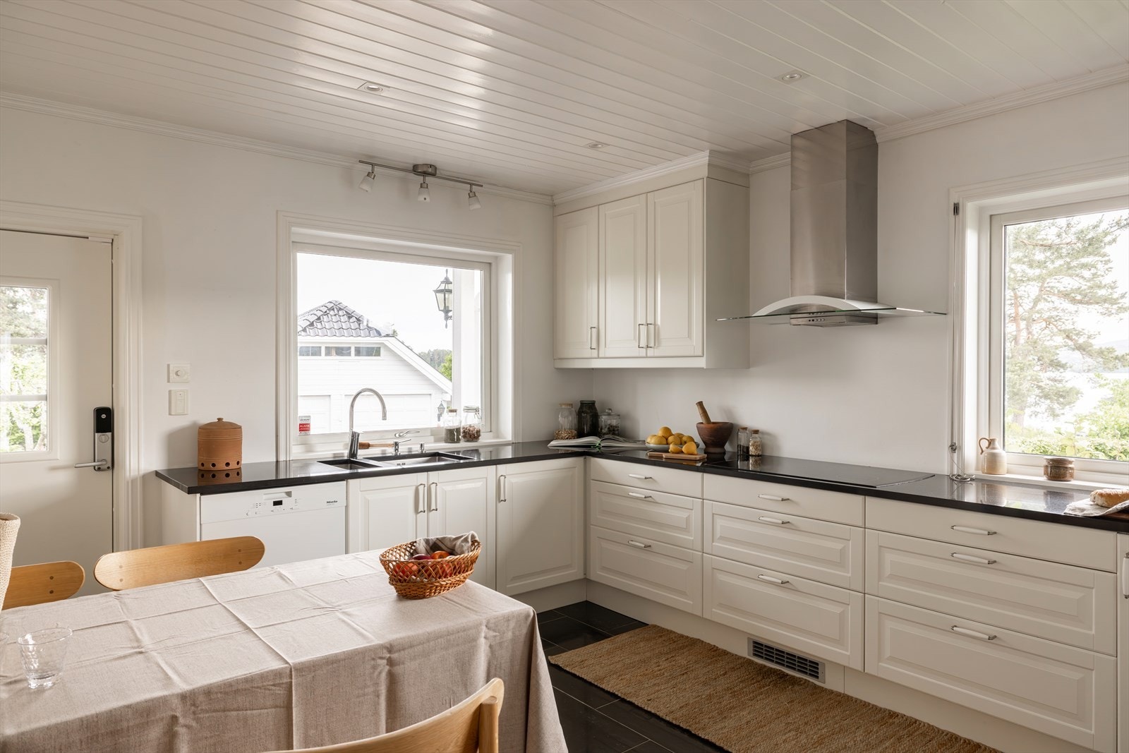 Lyst og klassisk kjøkken med hvite, profilerte fronter og sort stein benkeplate som skaper et tidløst og elegant uttrykk. Galleribilde