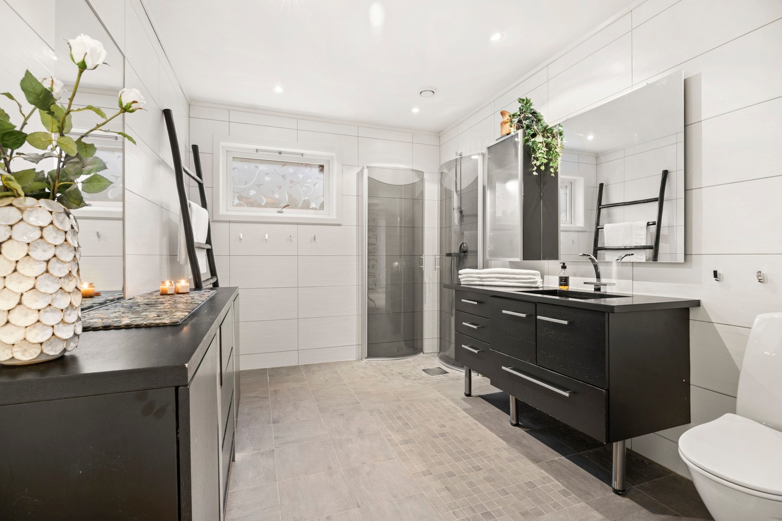 Bad i underetasjen med flislagte vegger og gulv, innredet med wc, dusjhjørne, servant integrert i skuffeinnredning, skap og speil Galleribilde