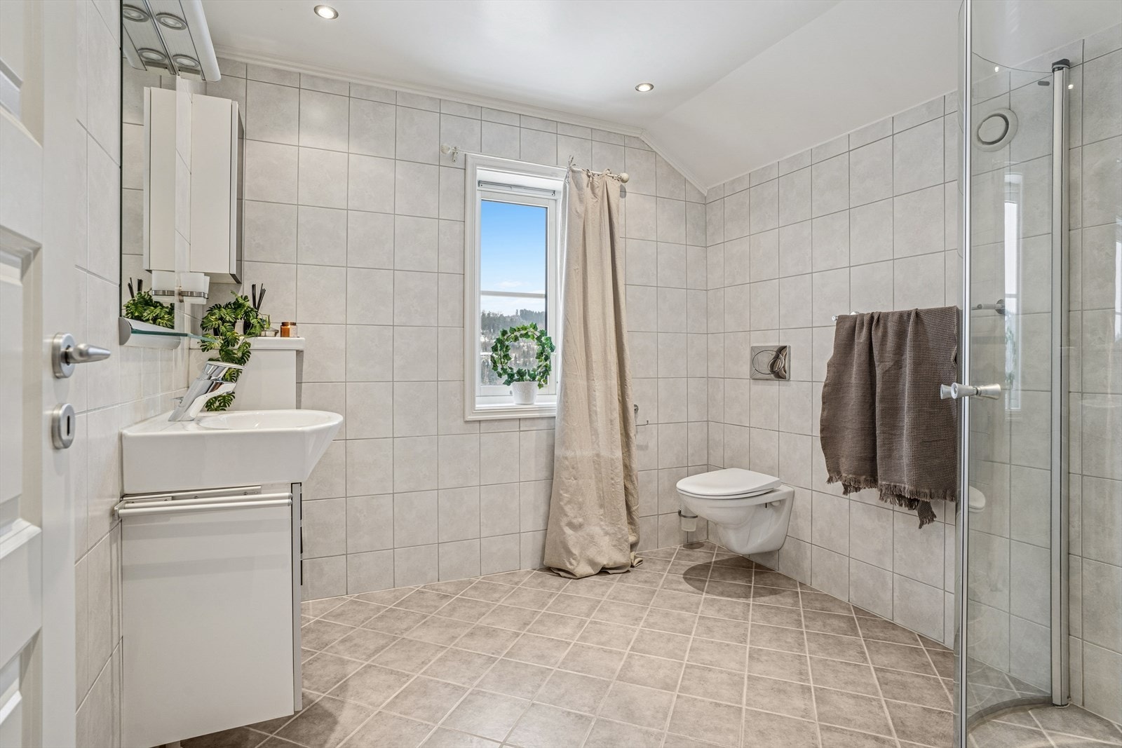 Badet er utstyrt med vegghengt toalett, dusjhjørne med glassvegger, samt baderomsinnredning med servant, blandebatteri og speil. Galleribilde