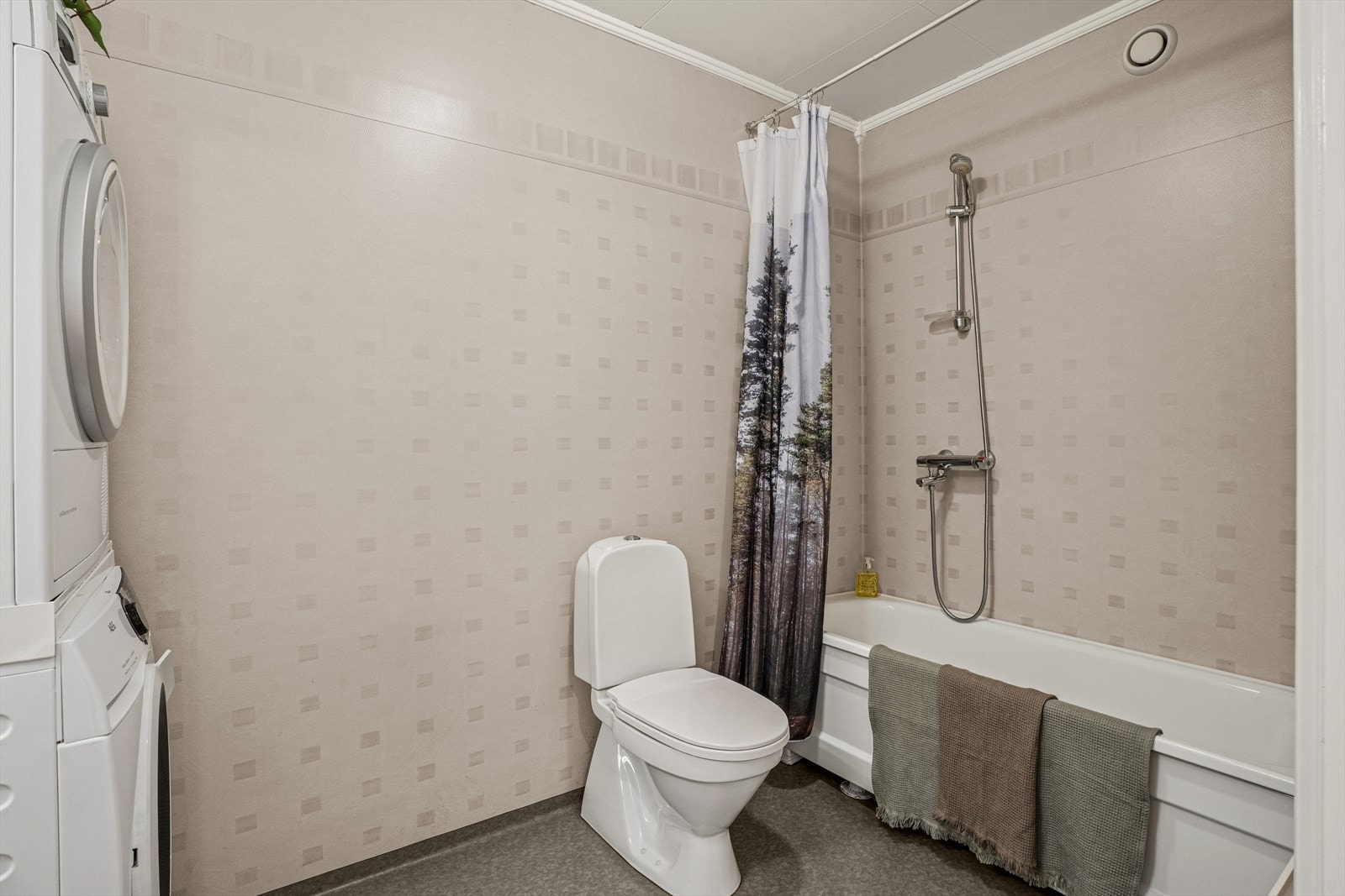 Badet er utstyrt med gulvmontert toalett, badekar med dusj, samt baderomsinnredning med servant, blandebatteri og speil. Galleribilde