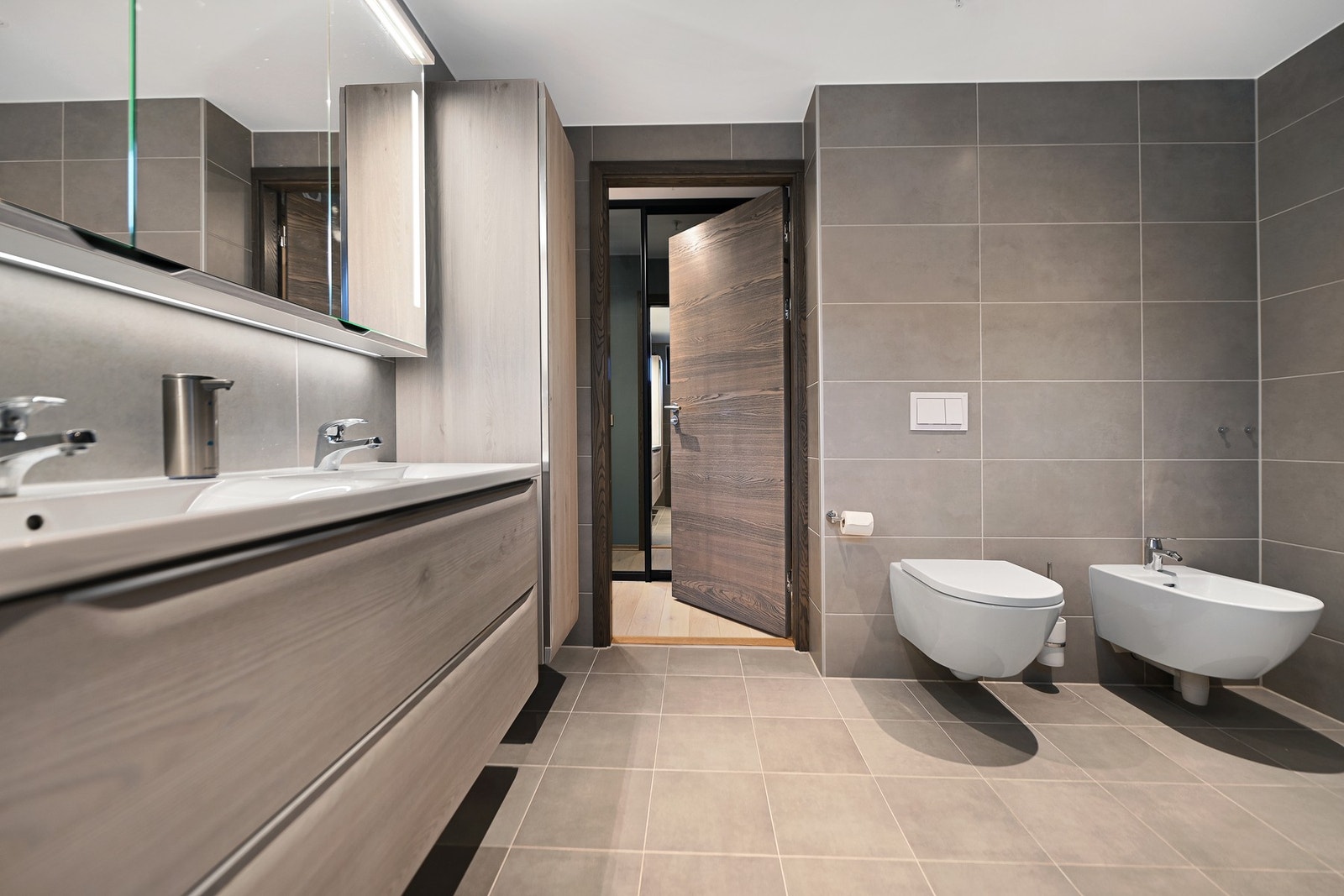 Rommet er innredet med to nedfelte servanter, veggfestet toalett, bidé og dusjhjørne. Galleribilde