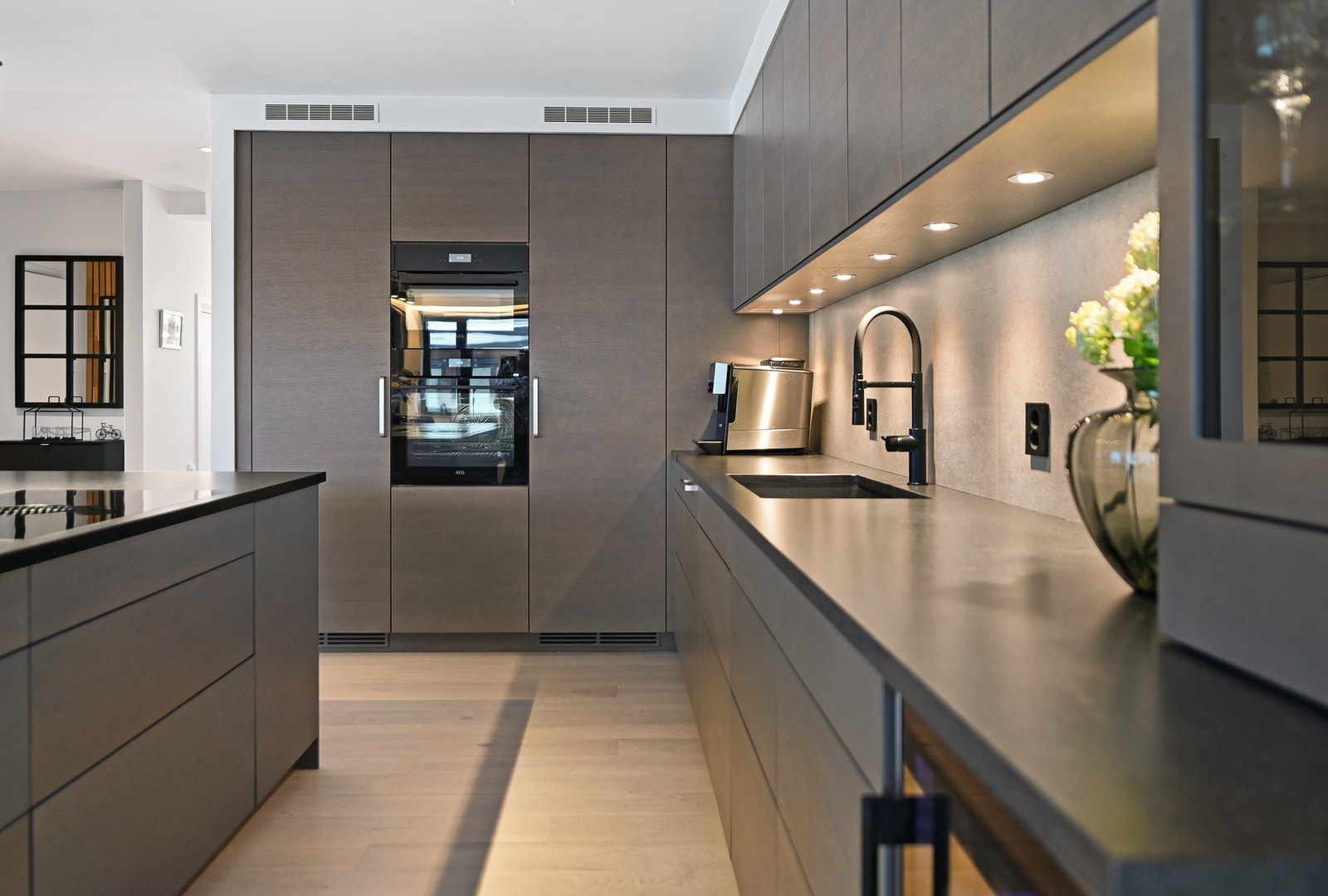 Langs bakveggen er det en lang praktisk kjøkkenbenk med vask og komfyr, og overskap til oppbevaring. Galleribilde