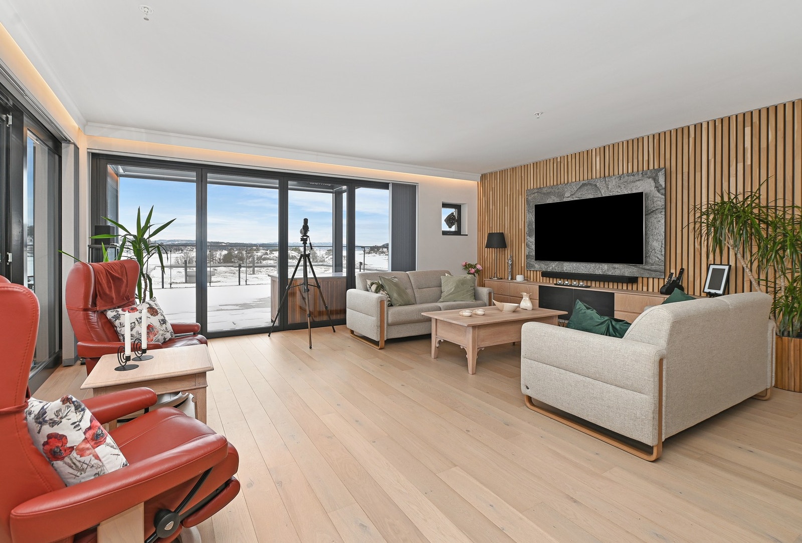 TV-veggen er utformet med spilevegg i lakkert eik. På spileveggen er det montert skiferfliser, der farger og struktur går igjen i kjøkkeninnredningen og skaper en fin sammenheng mellom rommene. Veggmontert TV-benk er installert, og både skifer, TV-benk og Galleribilde