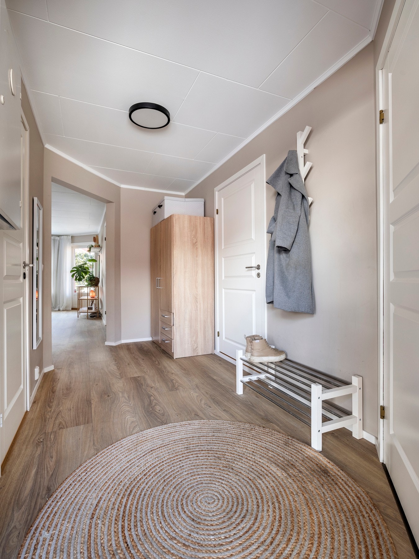 Entre med malte vegger i moderne fargetoner og laminatgulv. Entréen er innredet med et praktisk garderobeskap. Galleribilde