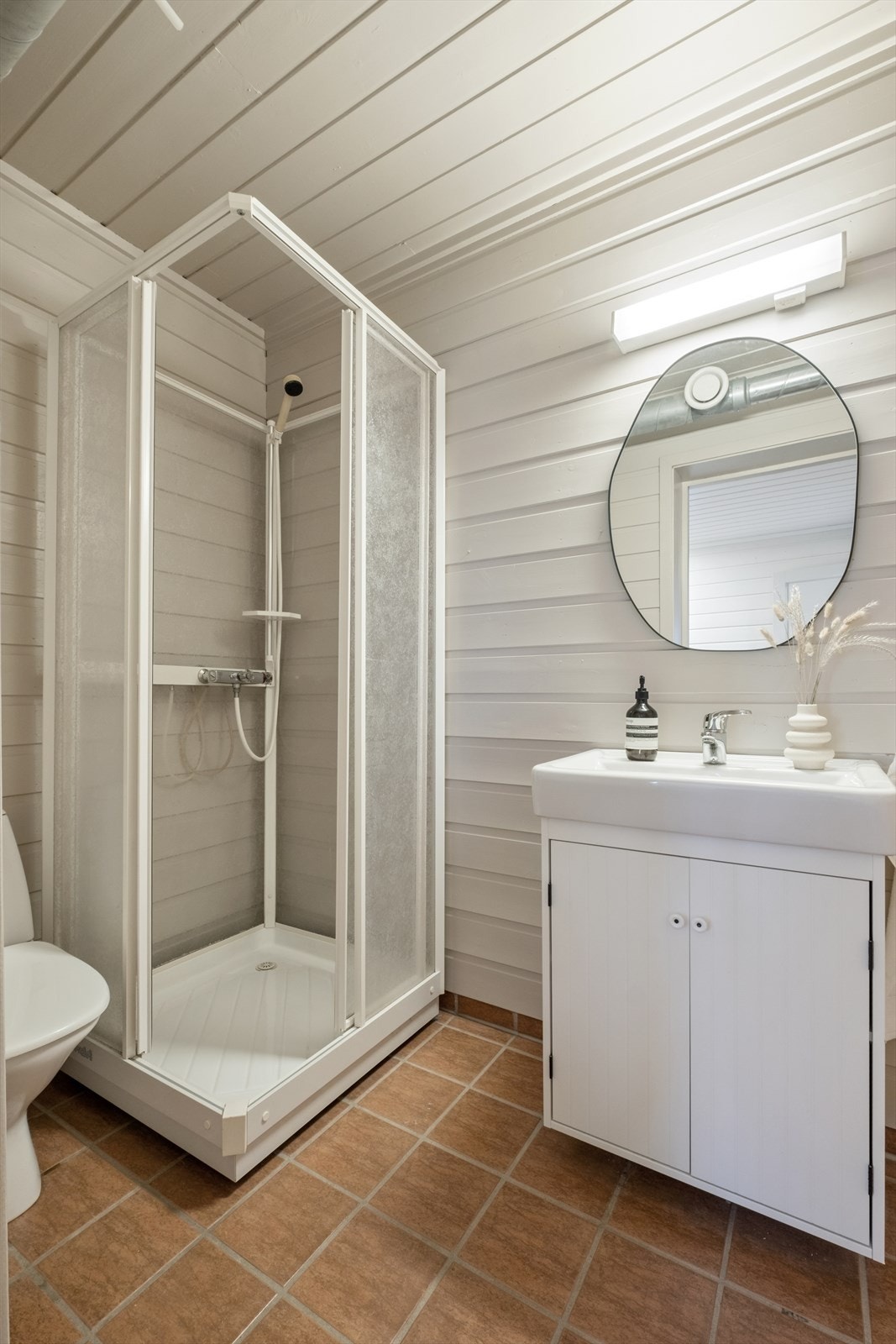 Badet i underetasjen har fliser på gulvet og trepanel på veggene. Det er utstyrt med servant, toalett og dusjkabinett for en praktisk løsning. Galleribilde