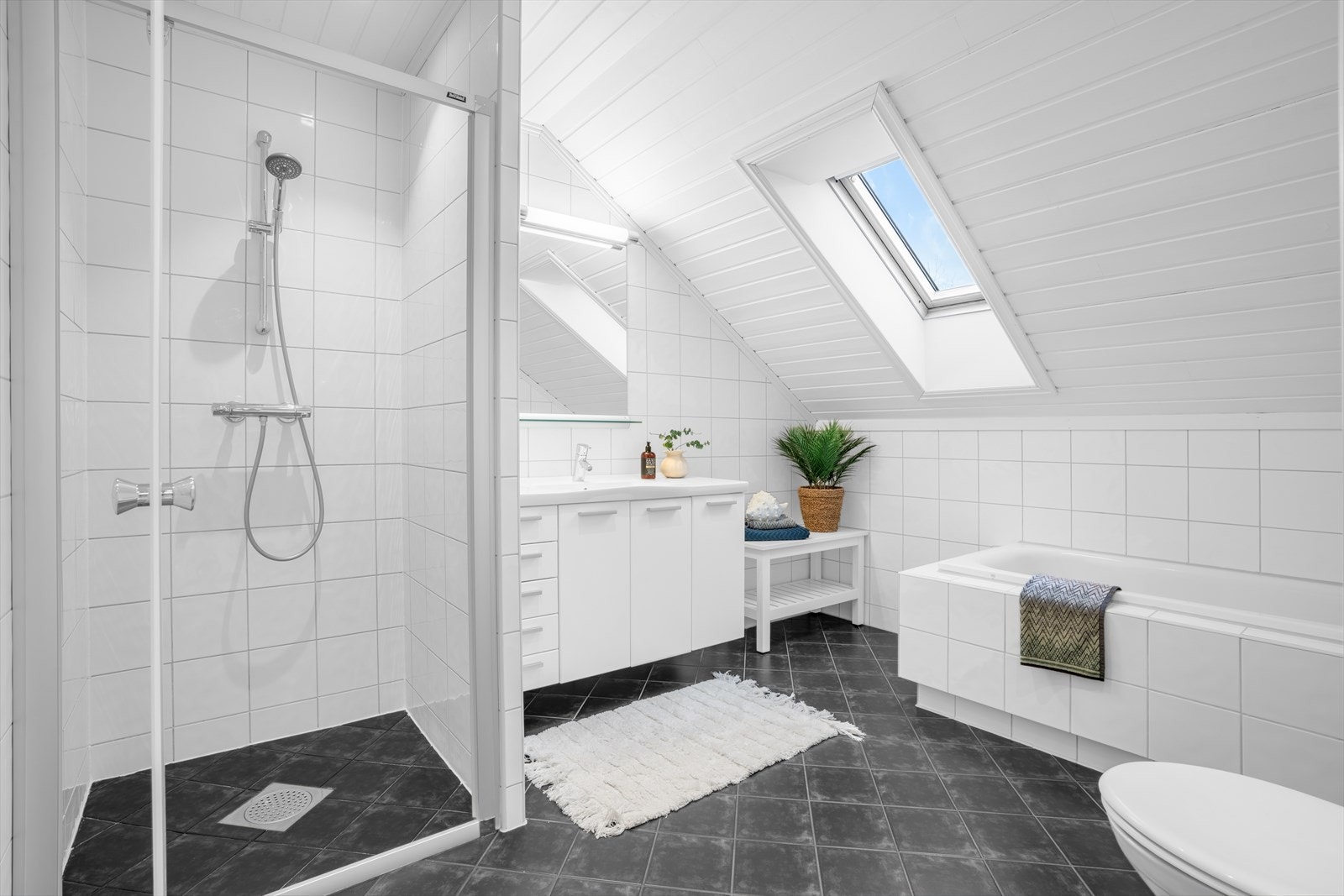 Flislagt bad i 2. etasje med gulvstående klosett, badekar og et dusjhjørne med dører i herdet glass. Galleribilde