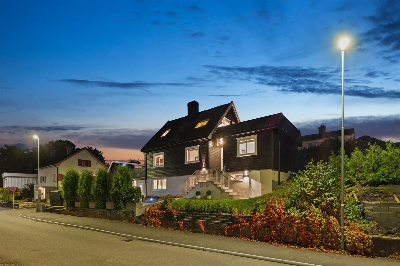 Fasaden tar seg spesielt godt ut når kvelden senker seg, og boligen fremstår med et varmt og innbydende uttrykk. Kveldsbildet viser tydelig hvordan eiendommen får et elegant og velstelt preg også etter mørkets frembrudd. Galleribilde