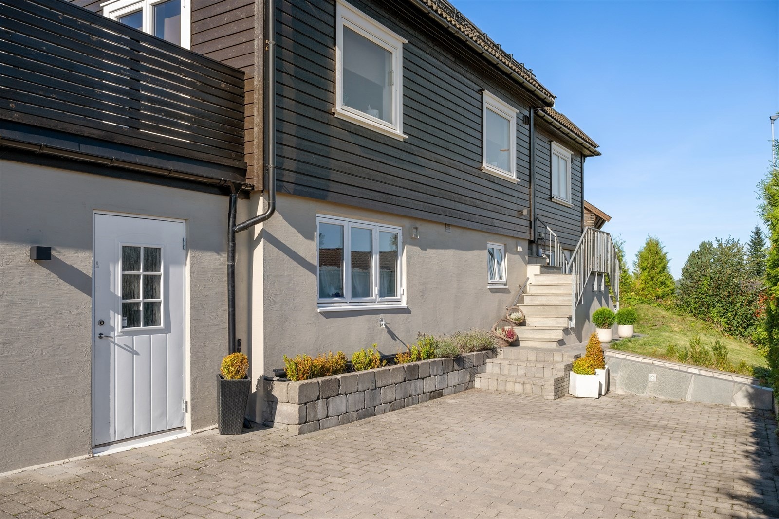 Foran huset møtes du av en opparbeidet og pen innkjørsel belagt med belegningsstein og belysning. En solid betongtrapp leder deg til hoveddøren og leiligheten i underetasjen har egen inngangsdør på bakkeplan. Galleribilde