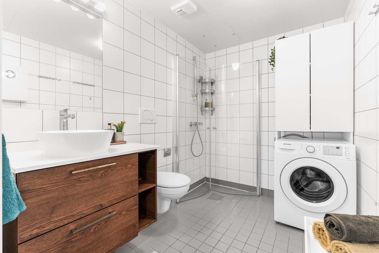 Lyst og pent flislagt baderom fra byggeår med baderomsinnredning som består av glatte, folierte fronter og servantbolle plassert på laminat benkeplate. Veggmontert toalett og dusj med innfellbare dusjvegger for god plassutnyttelse. Galleribilde