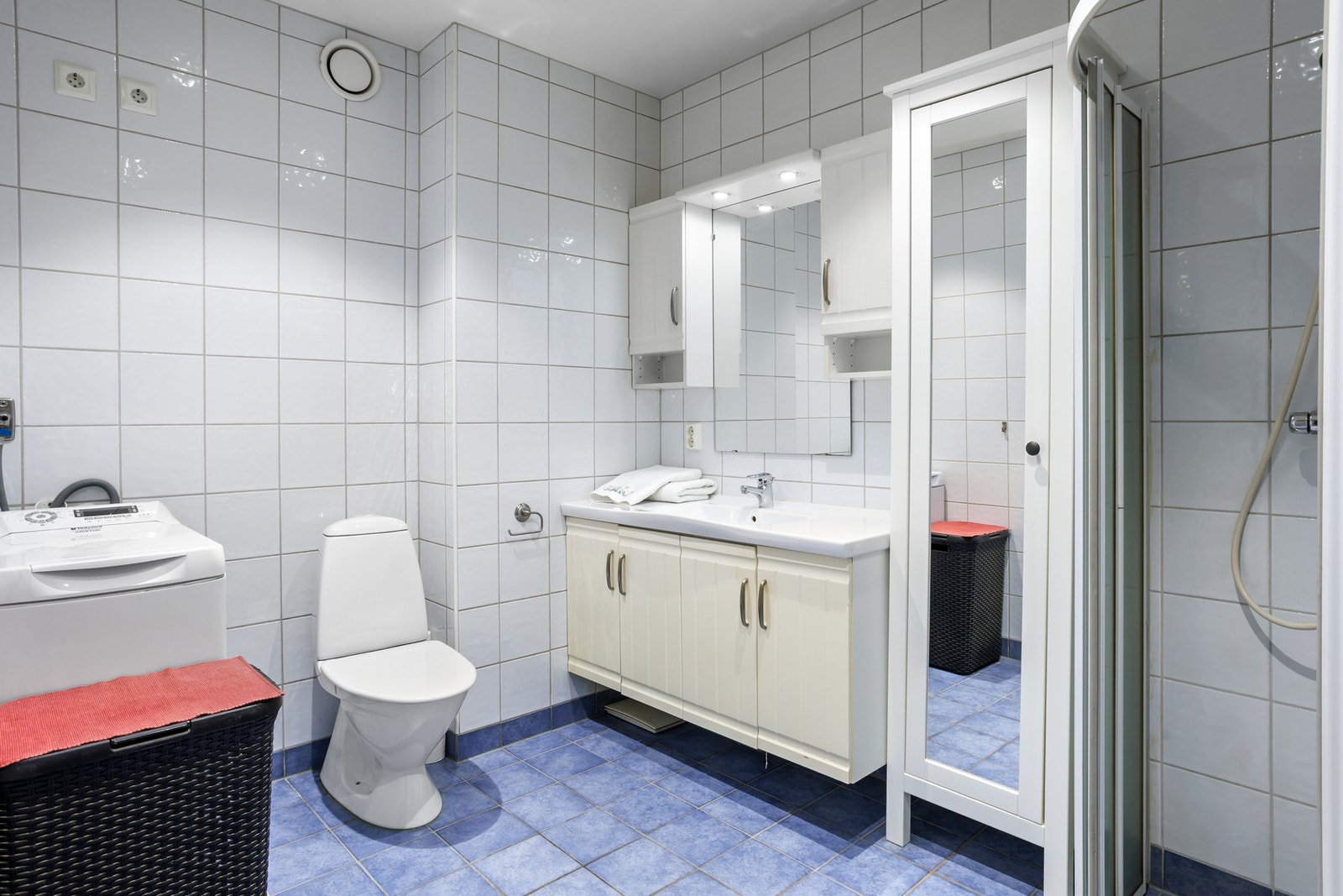 Flislagt bad med vegghengt servantinnredning, dushjørne og opplegg til vaskemaskin. Galleribilde