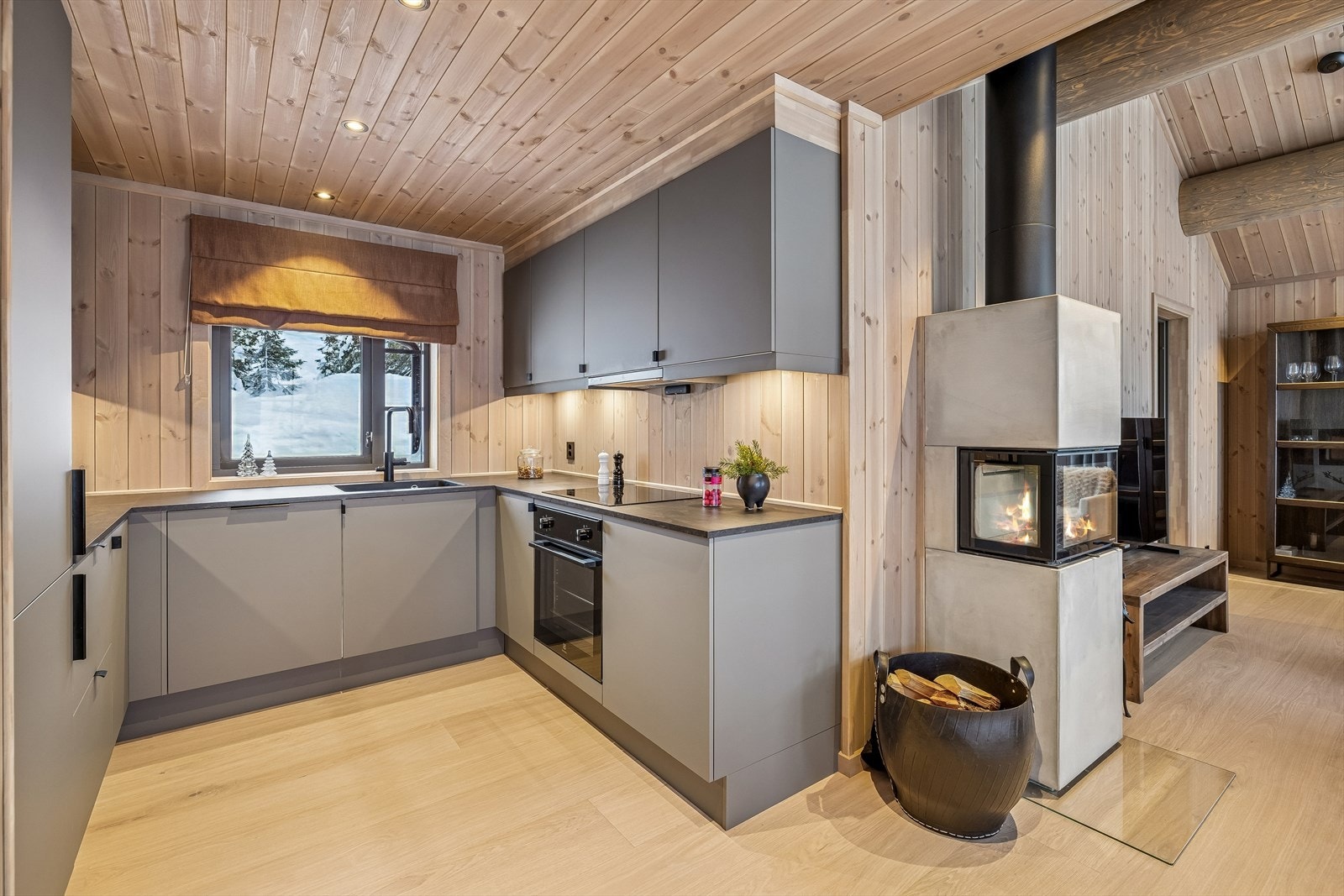 Det sosiale allrommet kombinerer et moderne kjøkken med en lun stue, sentrert rundt peisen. Galleribilde