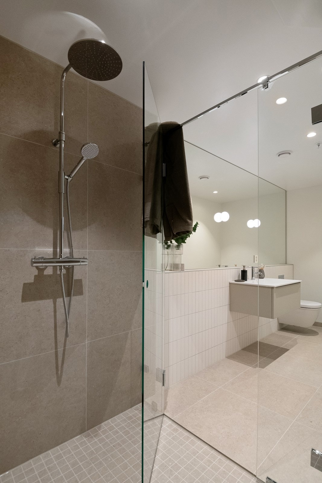 Her er det installert dusjnisje med veggmontert dusjdør/vegg og blandebatteri, innredning med heldekkende servant, speil med lys over servant og veggmontert klosett. Galleribilde