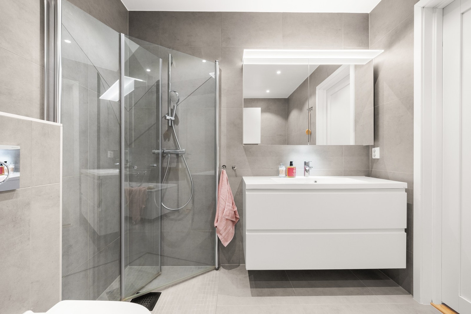 Badet er utstyrt med vegghengt toalett, badekar og dusjhjørne med innfellbare glassdører, en plassbesparende og stilren løsning som gir et luftig uttrykk. Galleribilde