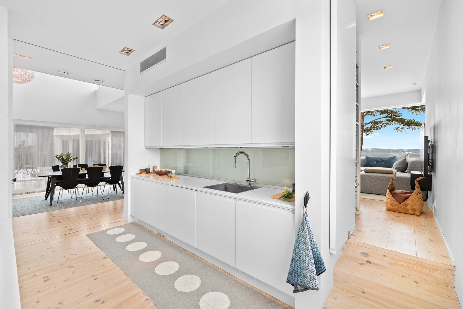 Smarte og fine løsninger er gjennomgående i hele boligen. Alt ifra skyvedørene som kan dele inn rommene i mer private soner (som går fra gulv til tak), passasjen mellom sonene til høyre i bildet, samt skjult oppbevaring bak glassfeltet over kjøkkenbenken. Galleribilde