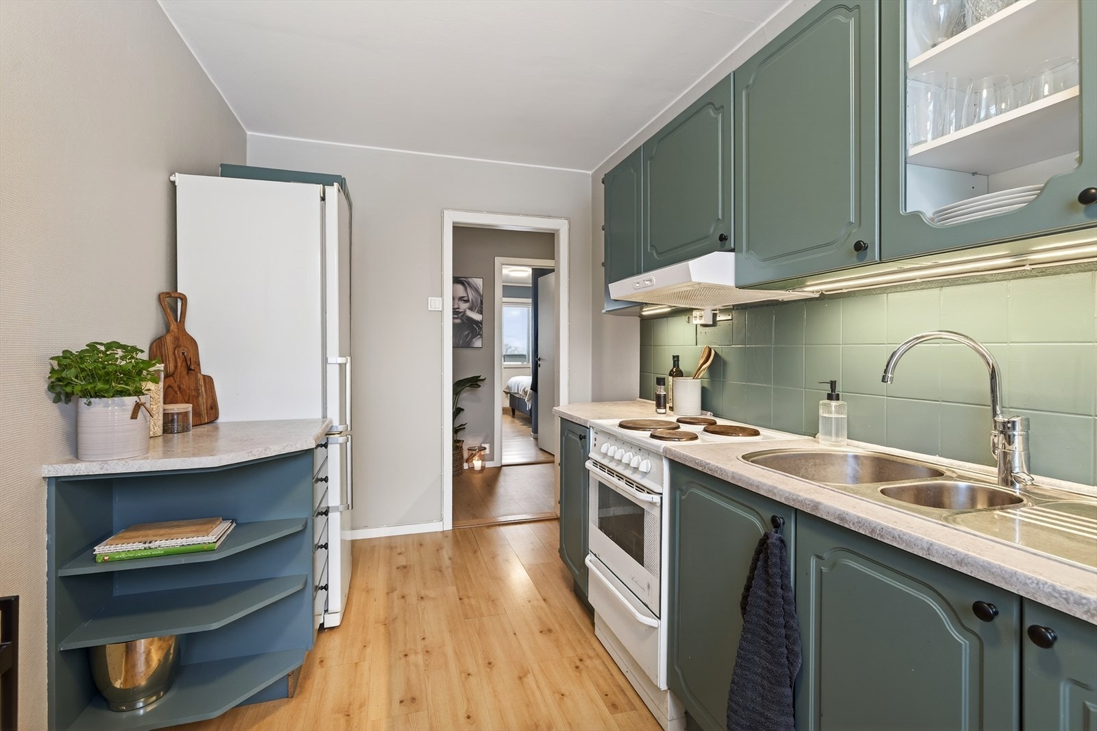 Pen kjøkkeninnredning med malte profilerte fronter og benkeplate av laminat. Det er fliser på vegg over benkeplaten. Galleribilde