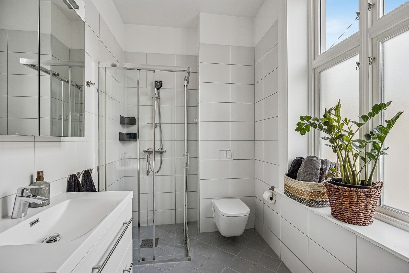 Delikat bad/WC med dusj og lukkede dusjdører, vegghengt toalett og servantskap. Galleribilde