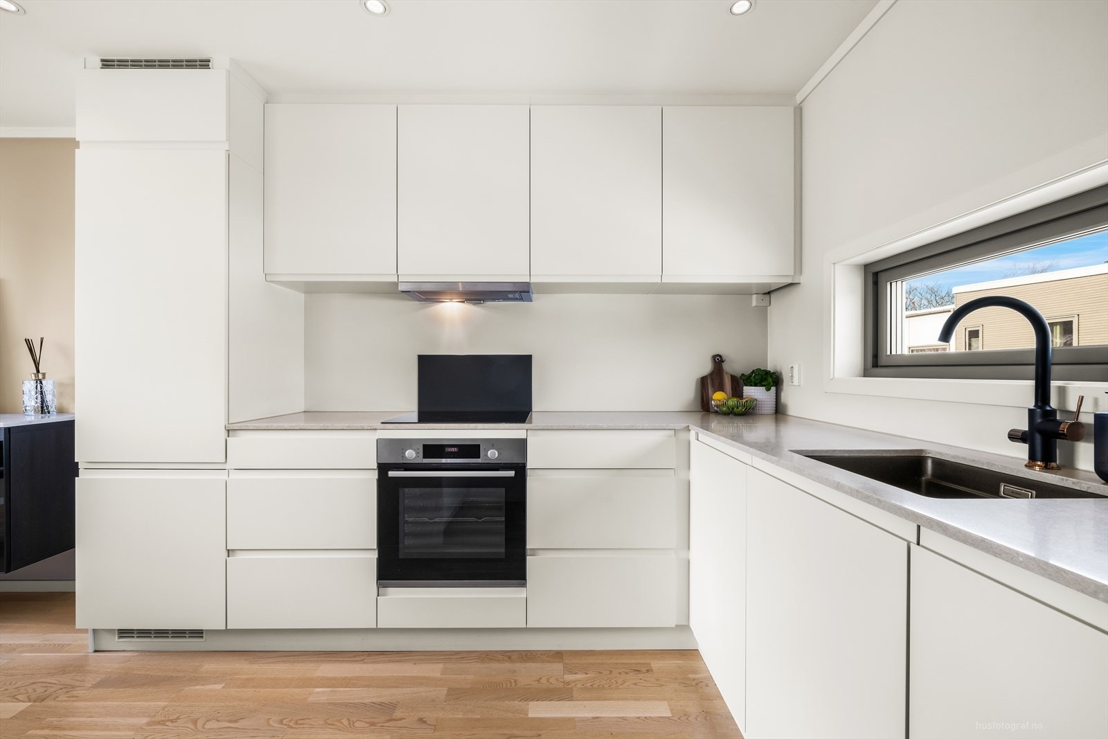 Kjøkkeninnredning med hvite slette fronter og benkeplate av kompositt. Galleribilde