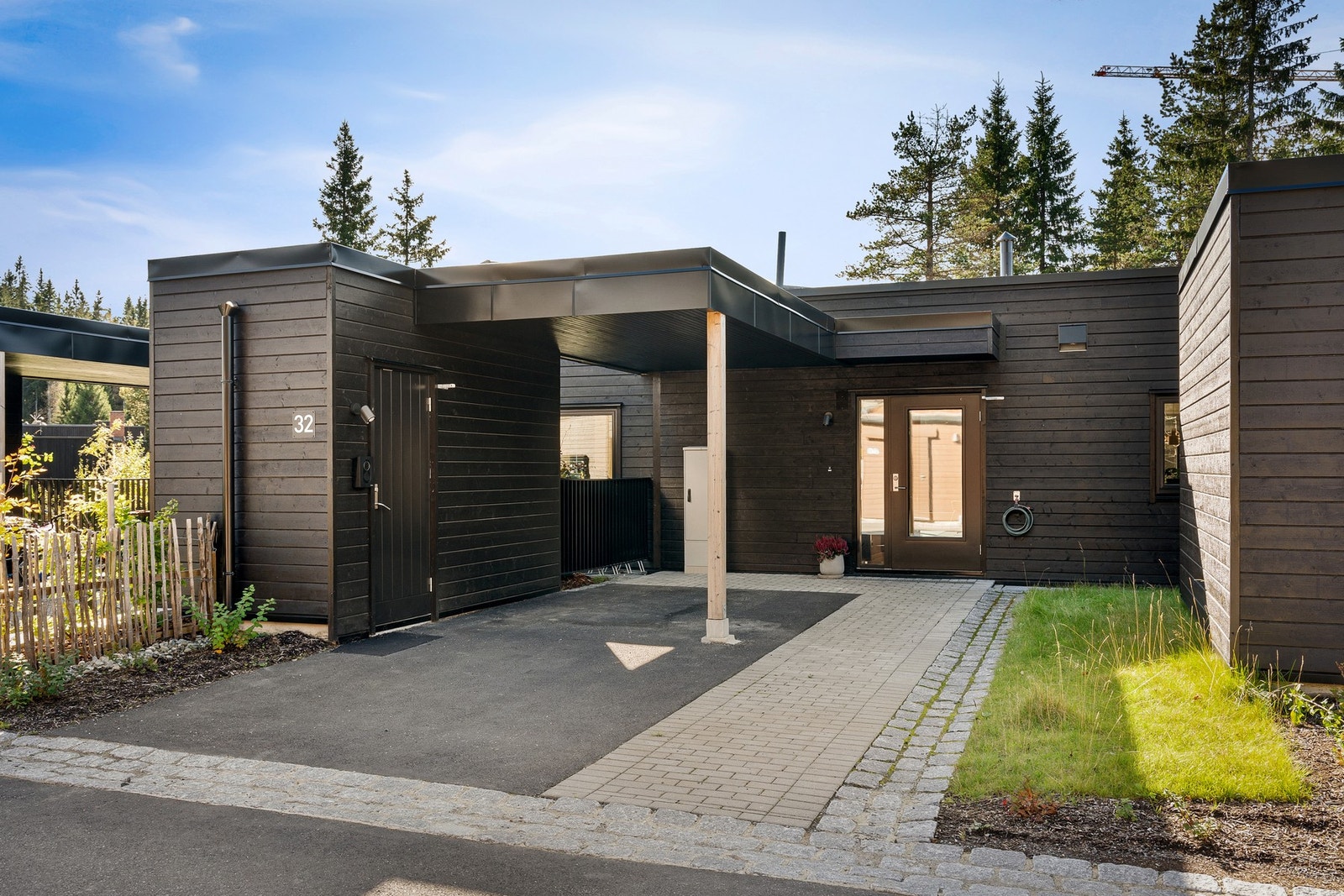 Praktisk inngangsparti med asfaltert carport m/elbillader, brosteinslagt sti frem til døren og en liten hageflekk som får morgensol. Galleribilde