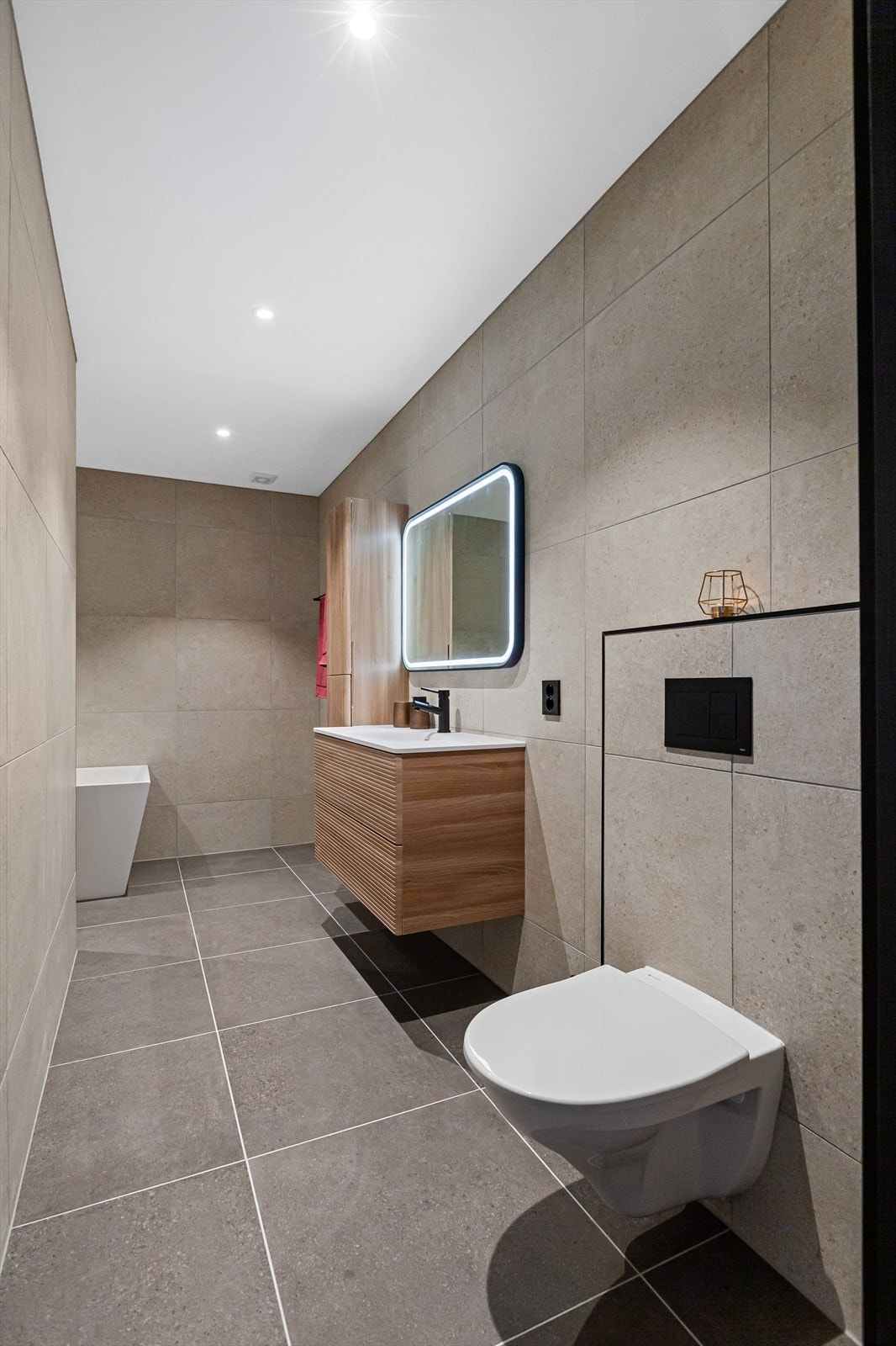 Flislagt bad utstyrt med servant, servantskap, mekanisk avtrekk, veggmontert wc, badekar og dusjnisje. Galleribilde