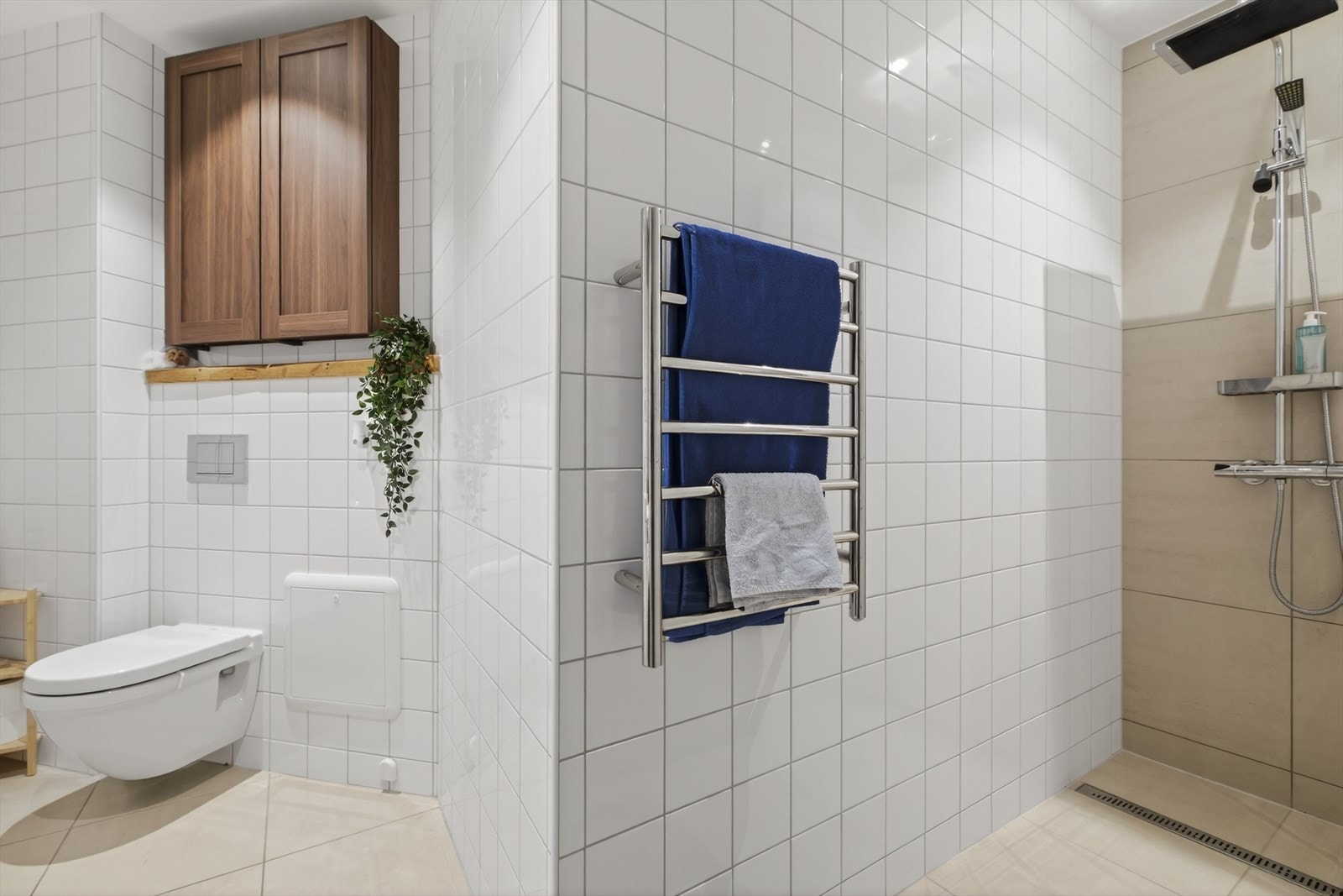 Badet er innredet med veggmontert toalett, servant med oppbevaringsskap, åpen dusjløsning, opplegg for vaskemaskin og skap for oppbevaring. Galleribilde