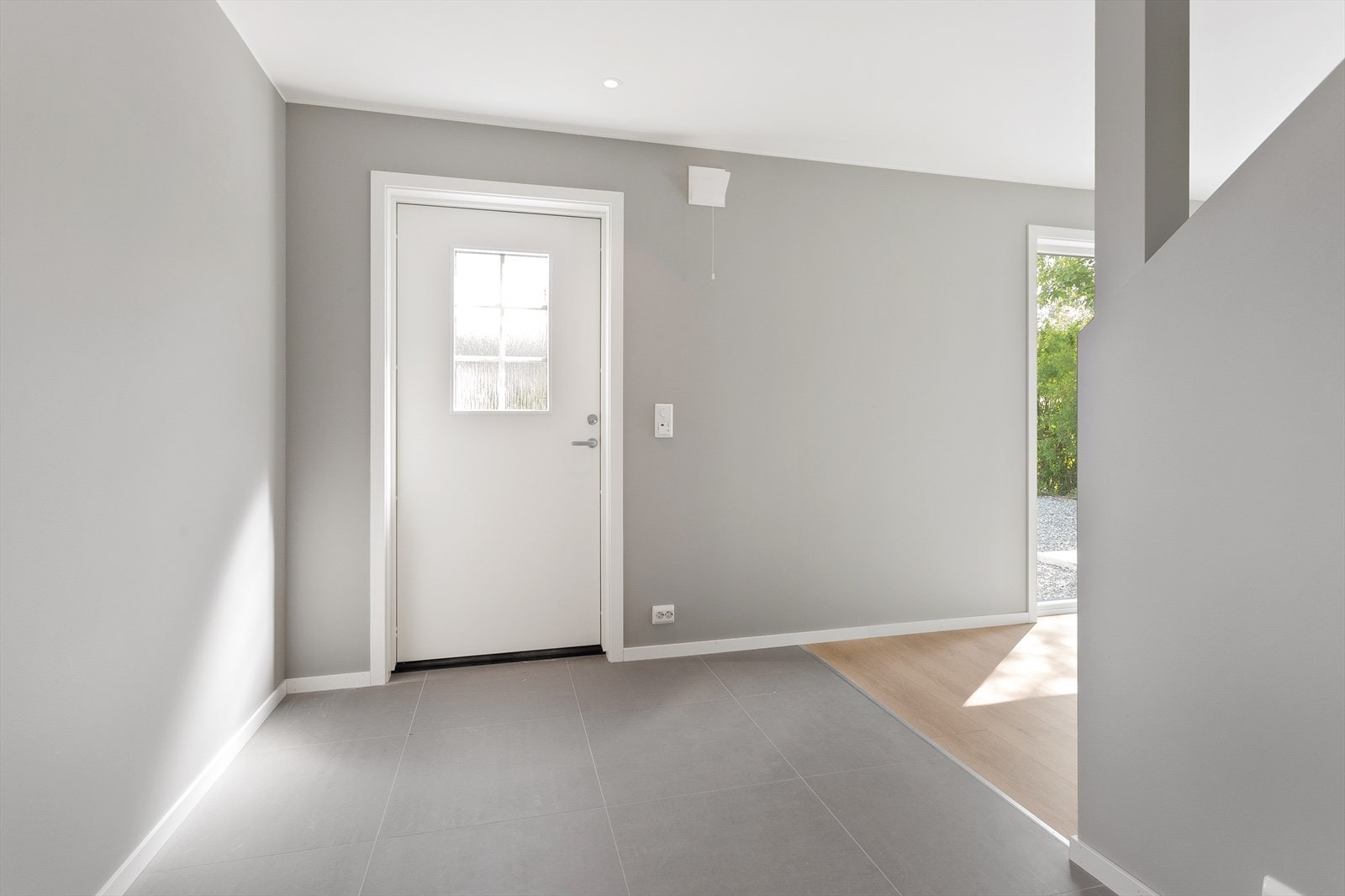Innenfor døren møtes du av en lys og innbydende entré med store, grå gulvfliser og harmoniske veggflater i samme stil. Galleribilde