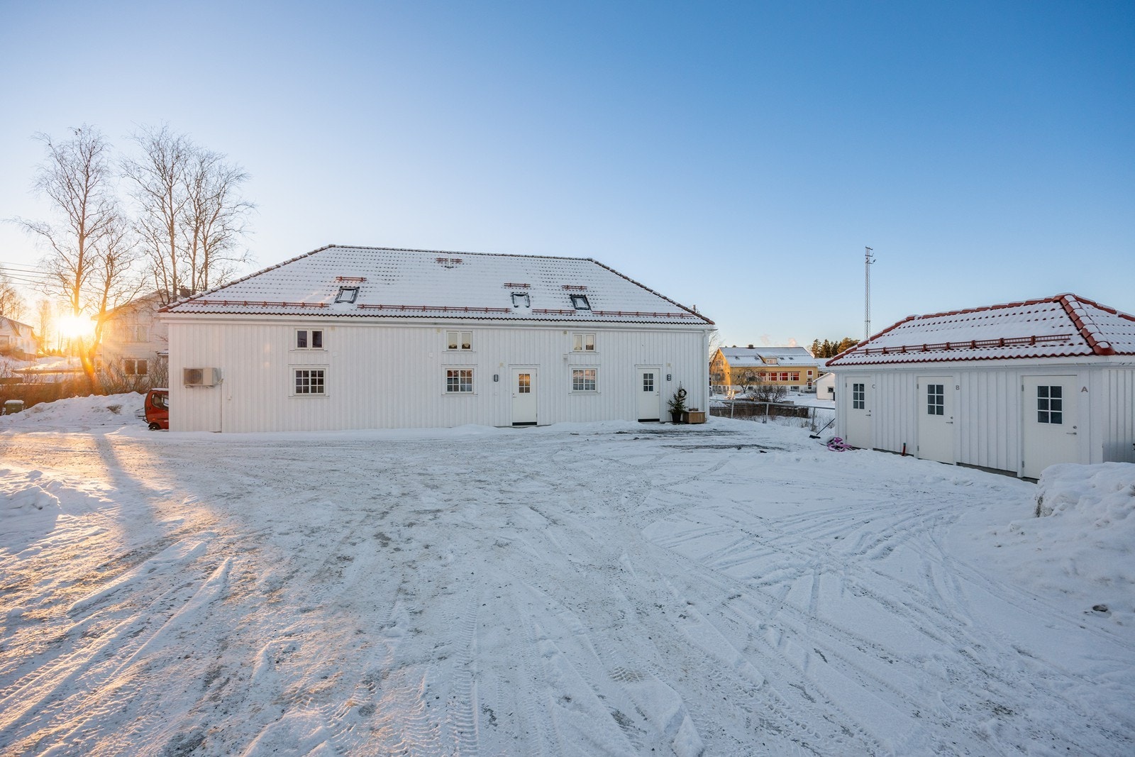 Rundt bygget har tomten trær, plen, naturlig vegetasjon og en stor, gruslagt gårdsplass for parkering. Galleribilde