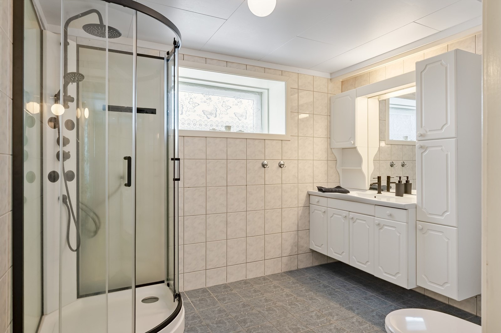 Lyst baderom i 1. etasje med fliser på gulv og vegger, elektrisk gulvvarme og avtrekksvifte. Galleribilde