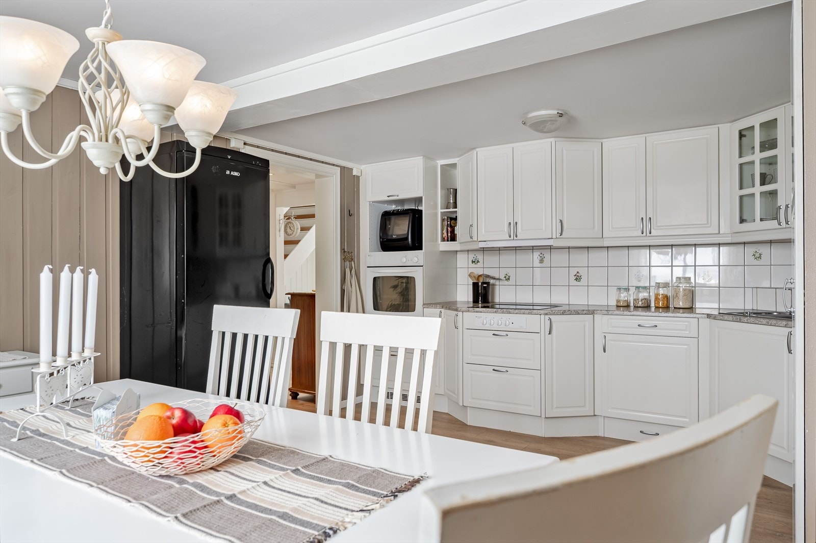 Kjøkkeninnredningen har lyse profilerte fronter og benkeplate med nedfelt oppvaskkum. Praktisk med lyse fliser i benkeryggen og belysning under de takhøye overskapene. Alle hvitevarer på kjøkkenet medfølger i handelen. Galleribilde