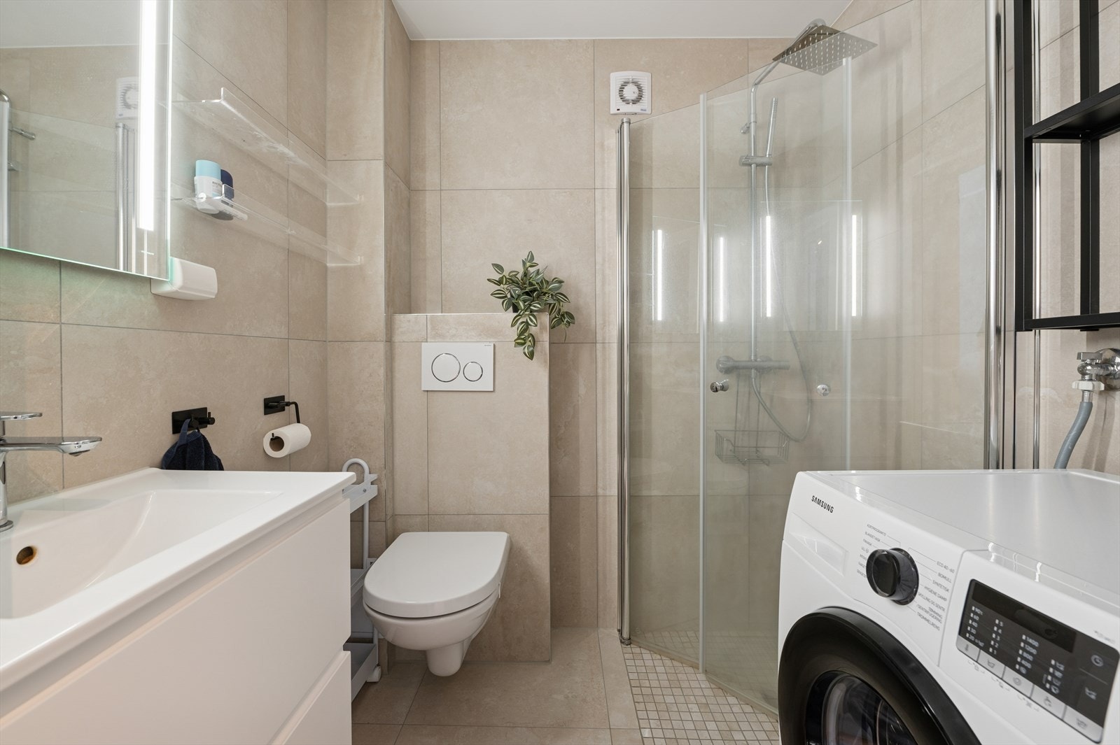 Delikat flislagt bad fra 2023. Rommet er utstyrt med dusjhjørne med regndusj og hånddusj, vegghengt toalett og opplegg for vaskemaskin. Galleribilde