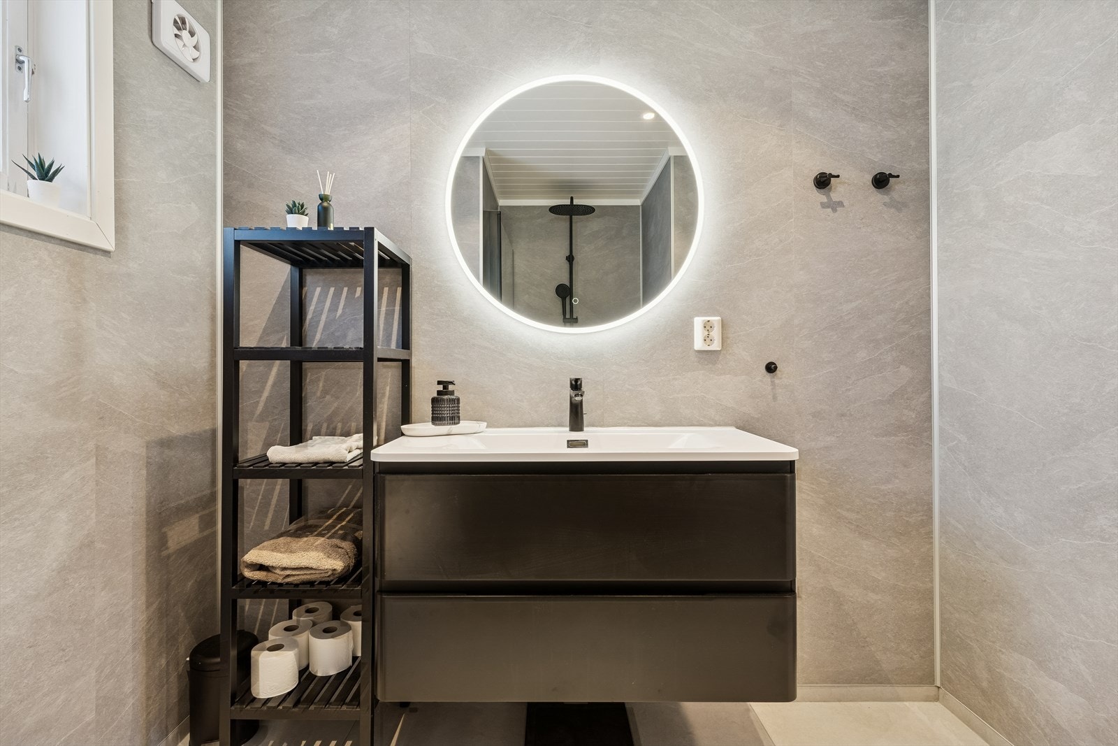 Baderomsinnredningen er i mørkt design med heldekkende servant og et stort speil med belysning. Galleribilde