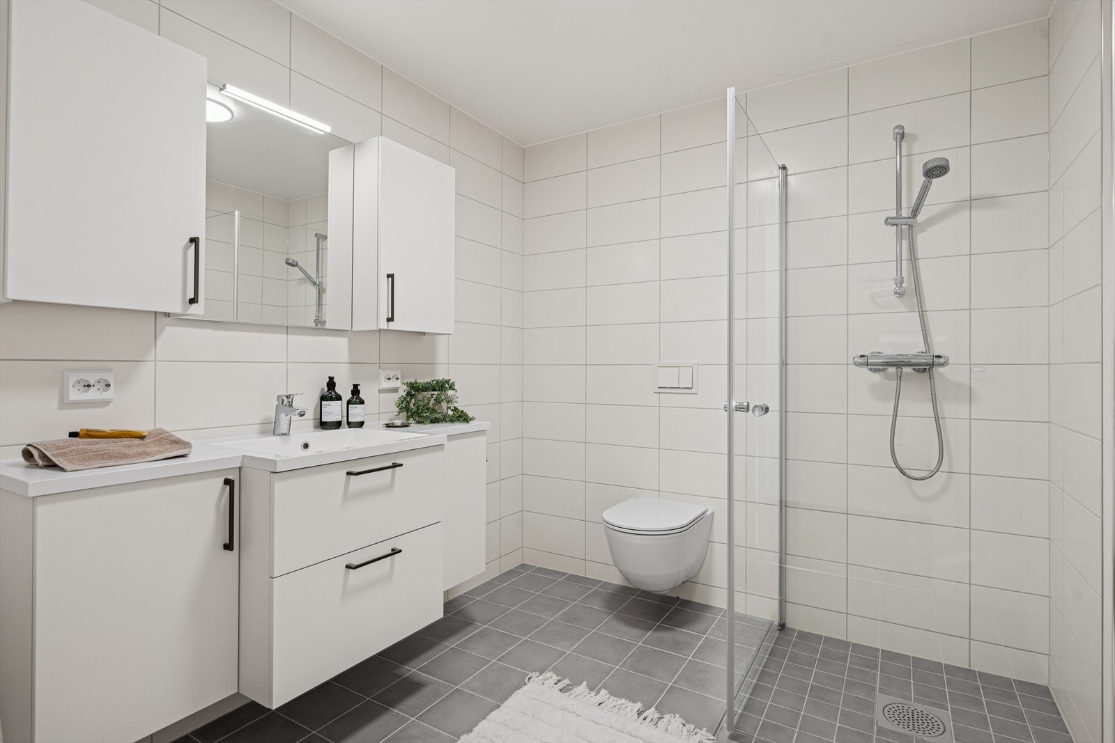 Det andre badet er innredet i tilsvarende stil og er utstyrt med dusjhjørne, vegghengt toalett og baderomsinnredning med god lagringsplass og nedfelt servant. Galleribilde