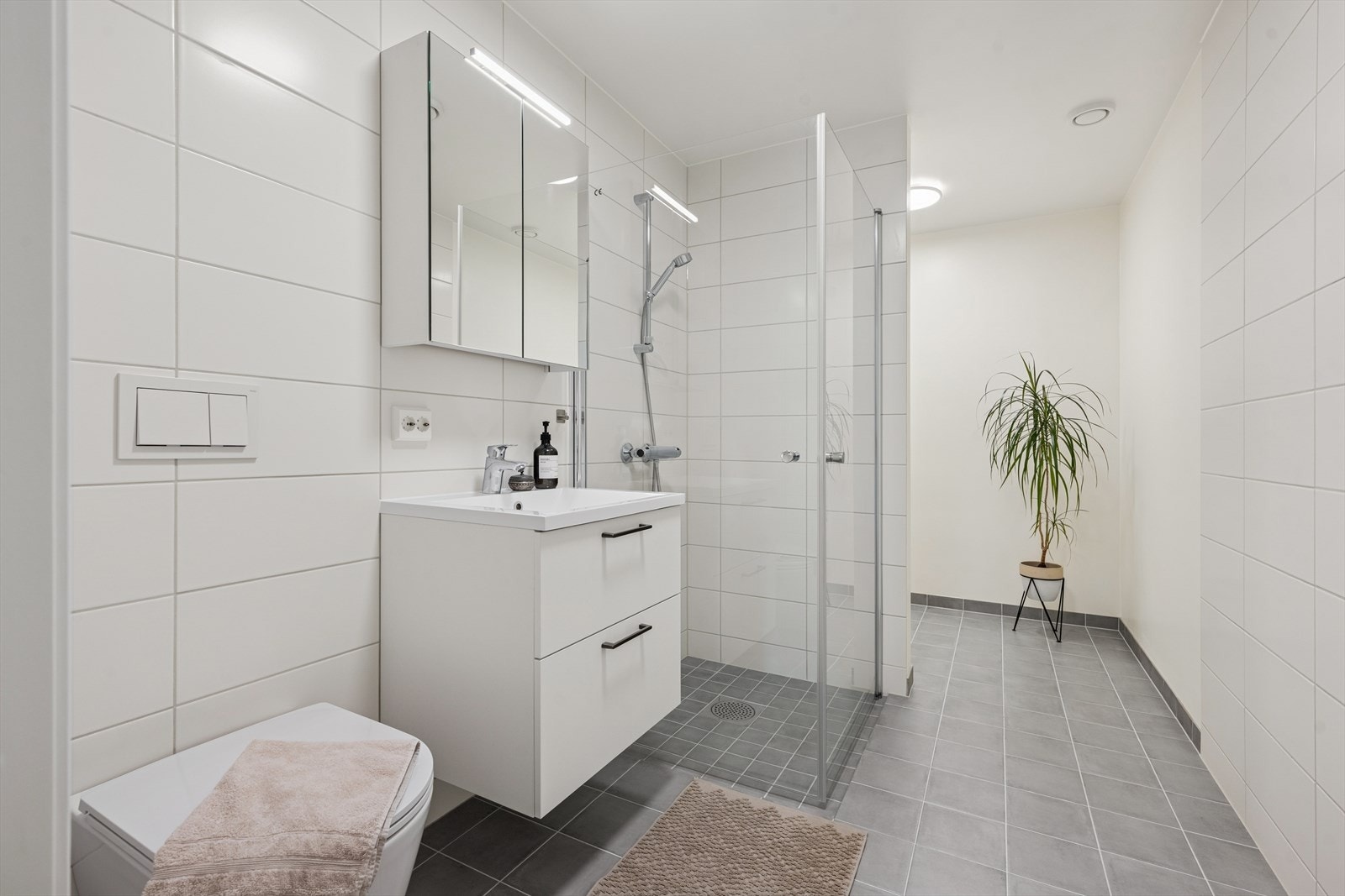 Det største badet er tidløst innredet med grå fliser på gulvet og hvite fliser på vegg. I gulvet har man også varme for ekstra komfort. Badet har opplegg til vaskemaskin bak halvvegg som skiller baderom og vaskerom. Galleribilde