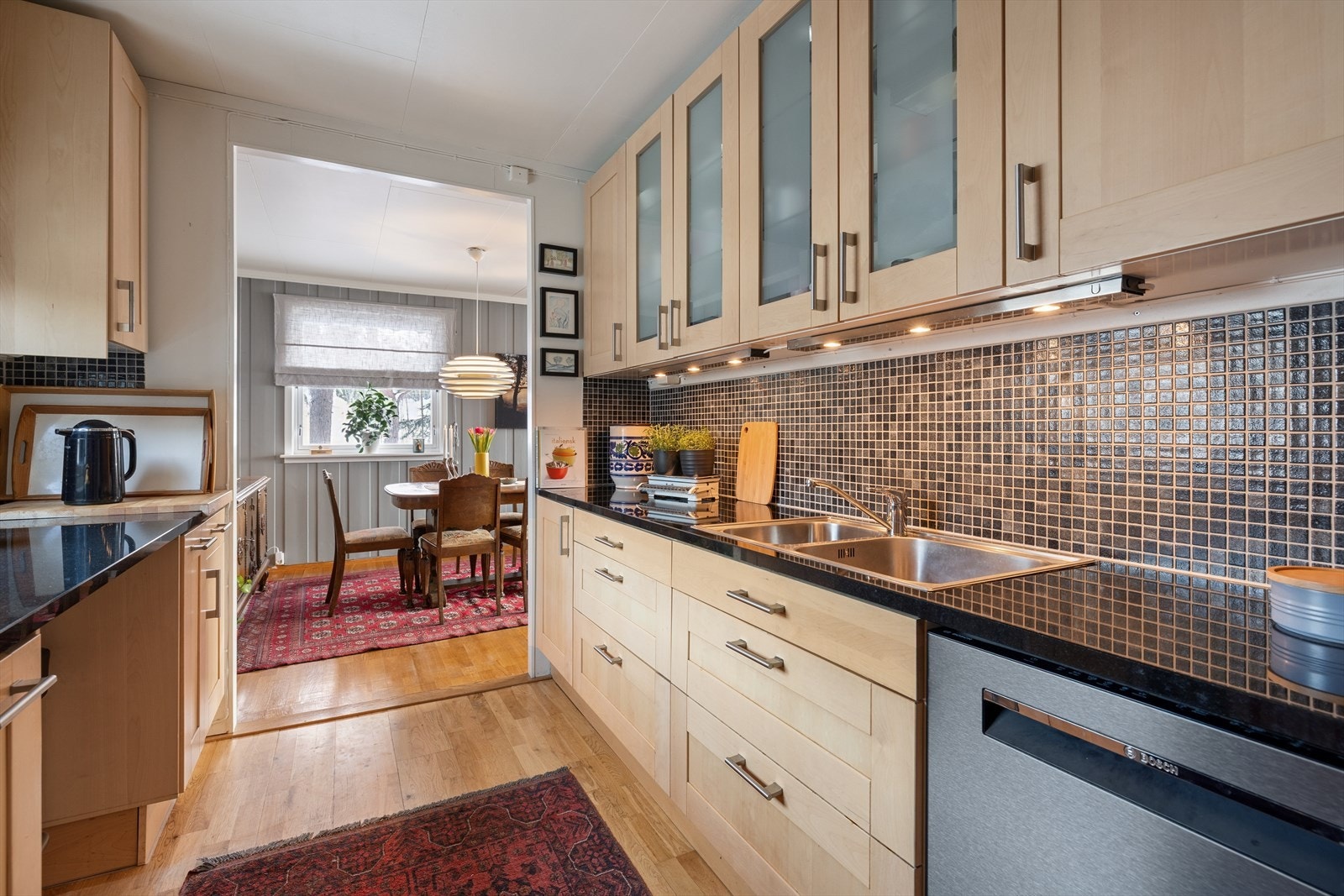 Kjøkkenet har en pen innredning med profilerte fronter og benkeplate i stein med nedfelt kjøkkenkum. Galleribilde