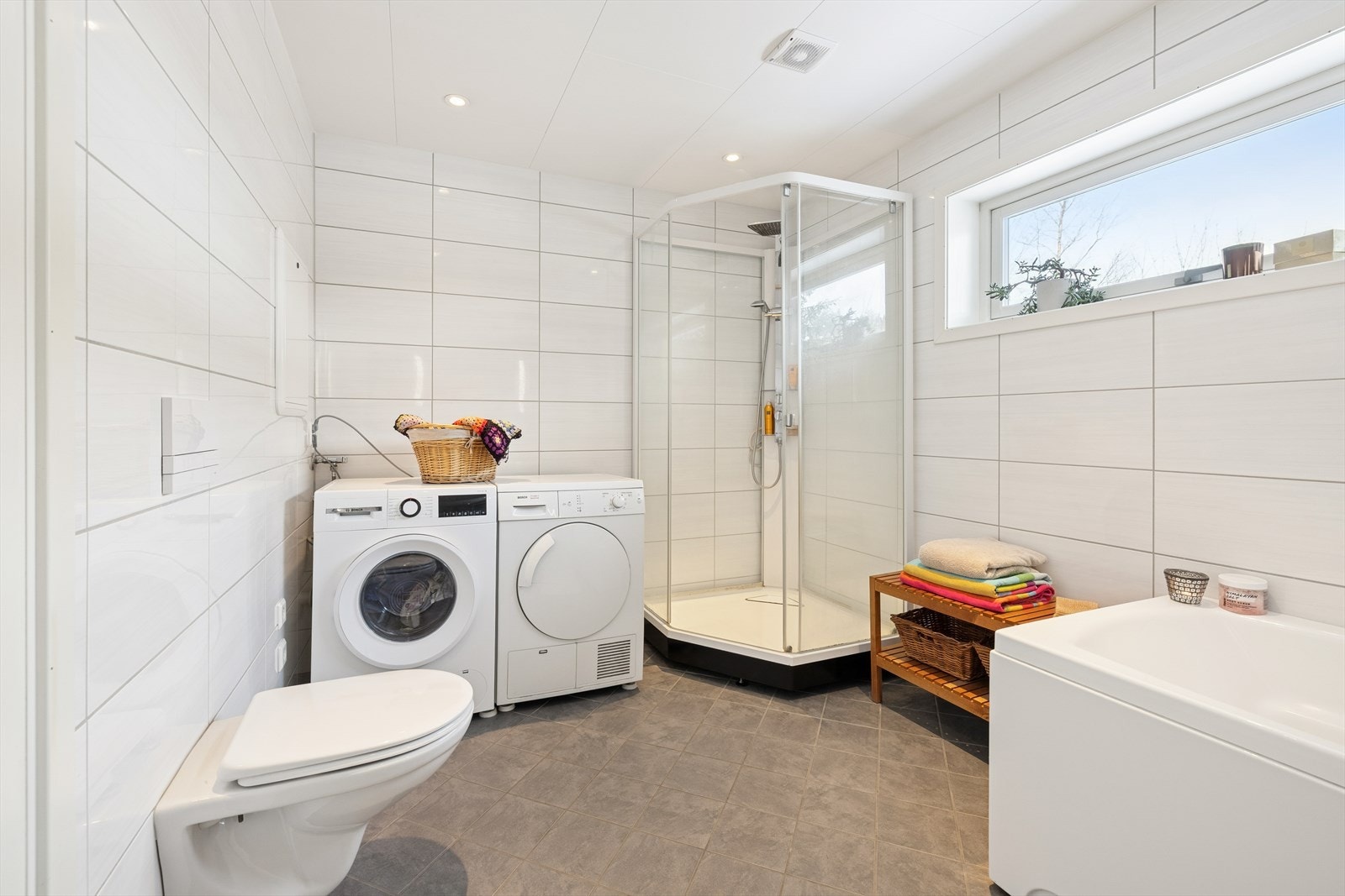 Badet er innredet med baderomsinnredning, speil med integrert belysning, veggmontert toalett, dusjkabinett og et deilig badekar. Det er også opplegg for vaskemaskin. Galleribilde