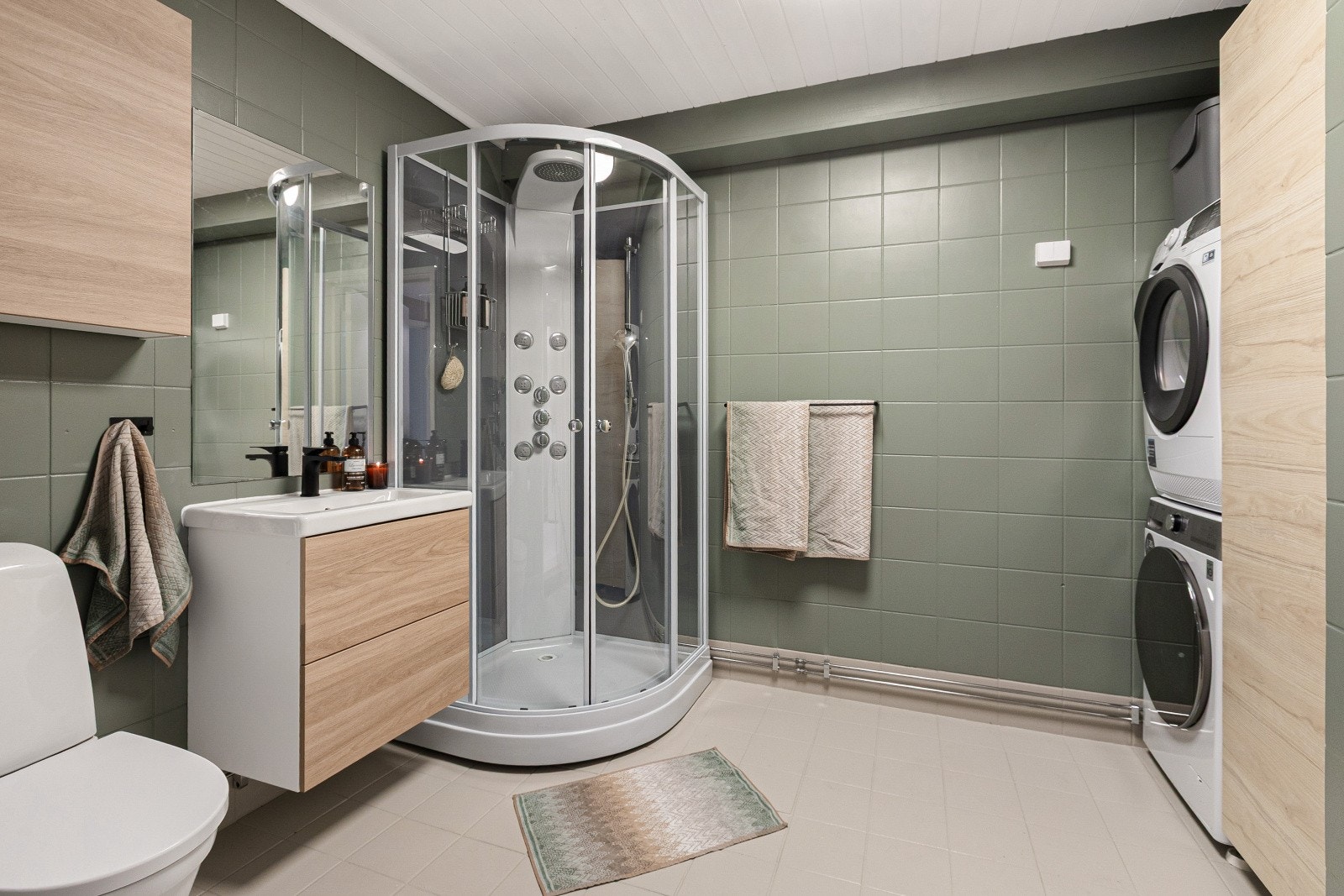 Baderommet i etasjen er utstyrt med malte fliser på gulv og vegger, servantinnredning med skuffeseksjon, ettgreps blandebatteri og speil. Det er behagelig gulvvarme i rommet, samt opplegg for vaskemaskin. Galleribilde