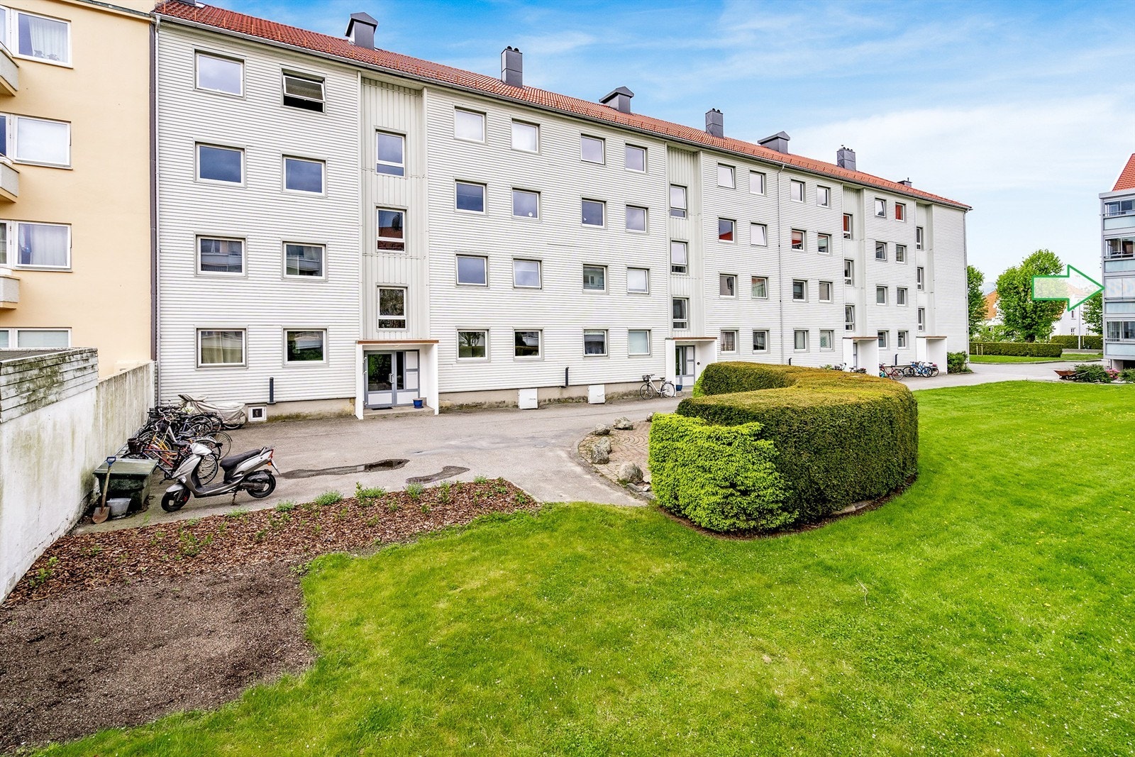 Fellesareal med benk og sykkelparkering. Pil markerer leilighetens plassering Galleribilde