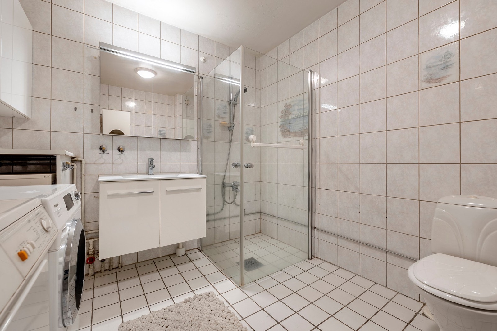 Baderomsinnredningen består av servantinnredning, diverse skap, toalett og dusjhjørne med svingbare glassdører. Galleribilde