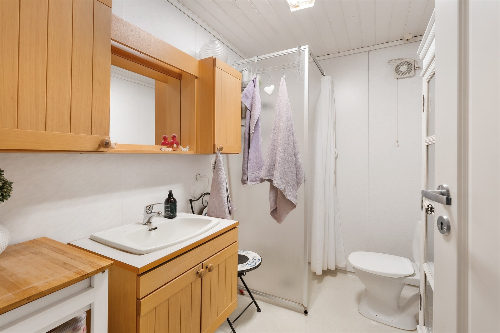 Badet er innredet med baderomsplater på vegger, belegg på gulv og panel i himling. Dusjnisje med forheng. Innredning med profilerte fronter og laminert benkeplate Galleribilde