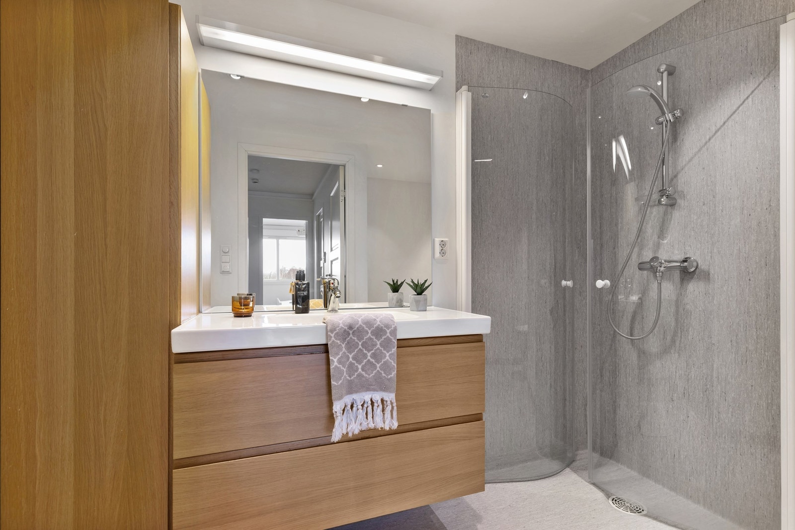 Badet ble oppgradert i 2011 og har en moderne innredning i eikefinish, stor servant og godt med oppbevaringsplass. Speilløsningen med lyslist gir rommet en lys og åpen følelse. Galleribilde