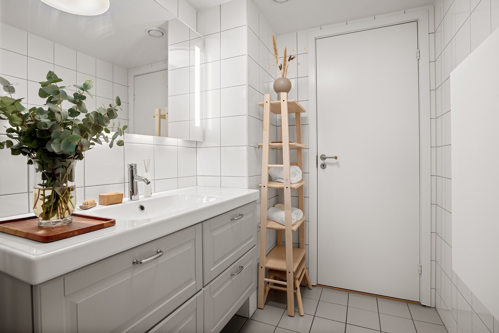 Badet er utstyrt med heldekkende servant, speil med lys, toalett, dusjkabinett og veggskap Galleribilde