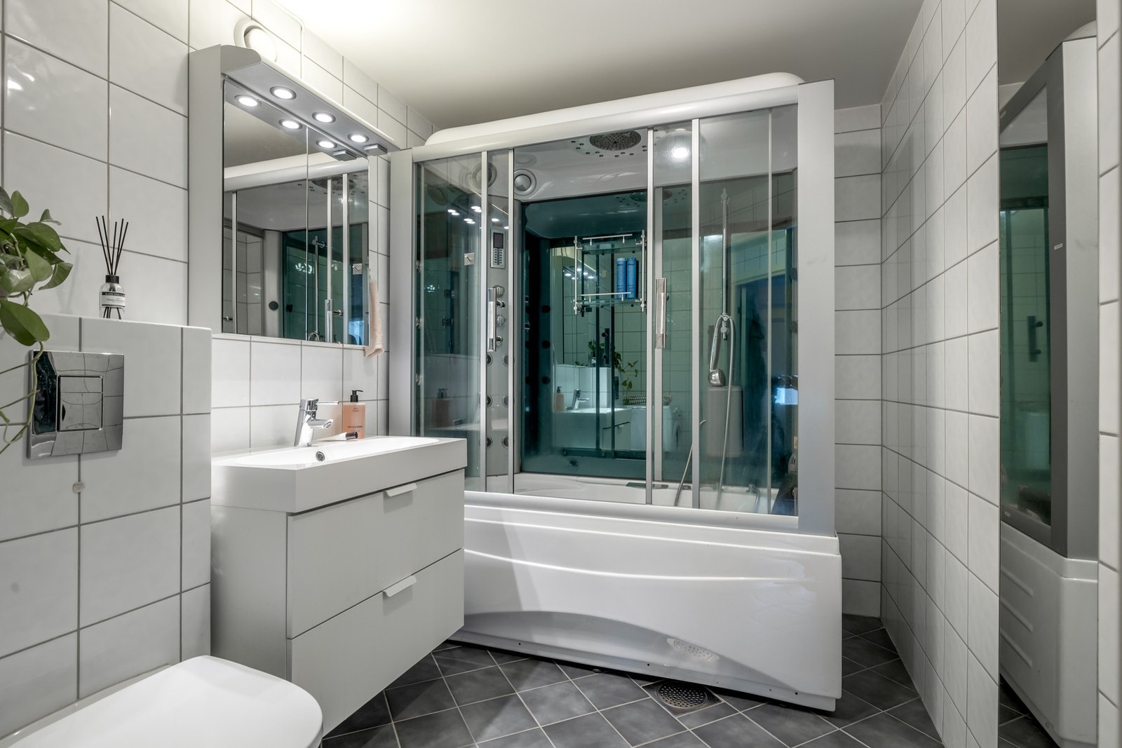 Badet er innredet med servantskap, heldekkende servant med ettgreps blandebatteri, speilskap med belysning, vegghengt toalett, lukket steambadekar med massasjefunksjon samt opplegg for vaskemaskin og tørketrommel. Galleribilde