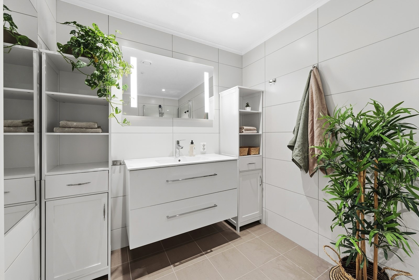 Badet er innredet med heldekkende servant over skuffeinnredning, speil med belysning, vegghengt toalett og dusjhjørne med innfellbare glassvegger Galleribilde