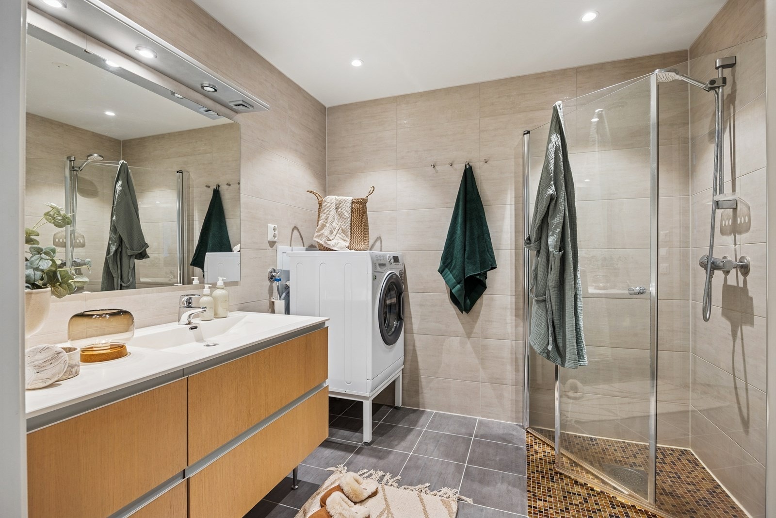 Badet er flislagt med behagelig gulvvarme. Øvrig innredning består av toalett, dusjhjørne m/innfellbare dører og en romslig baderomsinnredning med god plass til baderomsartikler. Galleribilde