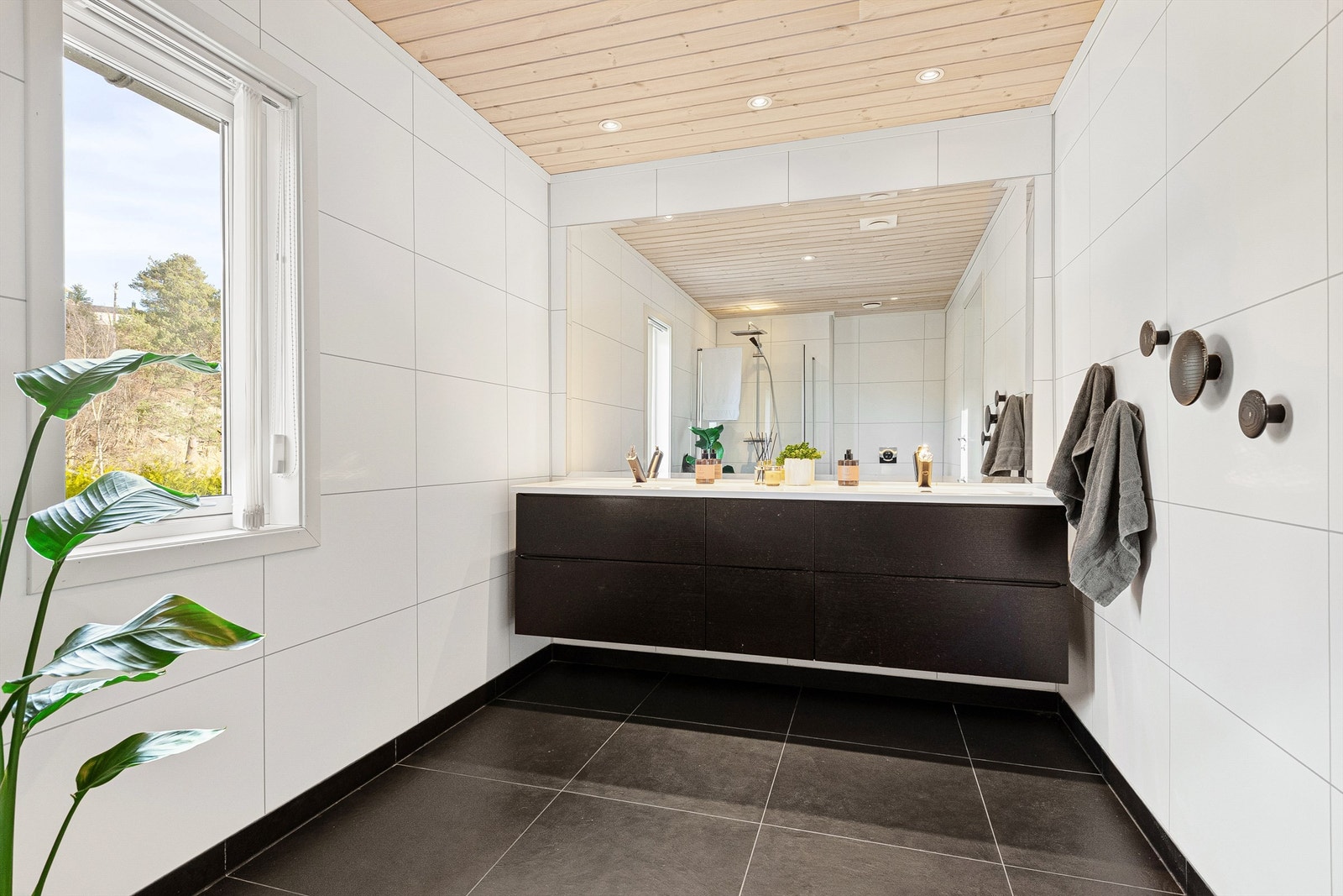 Stor baderominnredning med sorte fronter og skuffer med god oppbevaringsplass. Ovenpåliggende dobbel servant med ett-greps armaturer. Stort speil over servant. Galleribilde