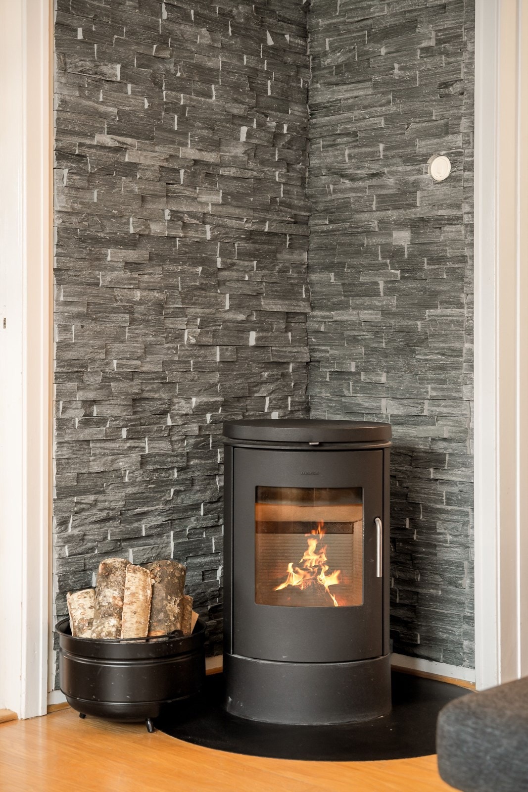Peisovnen plassert mot en dekorativ steinvegg skaper en lun og hyggelig atmosfære. Galleribilde