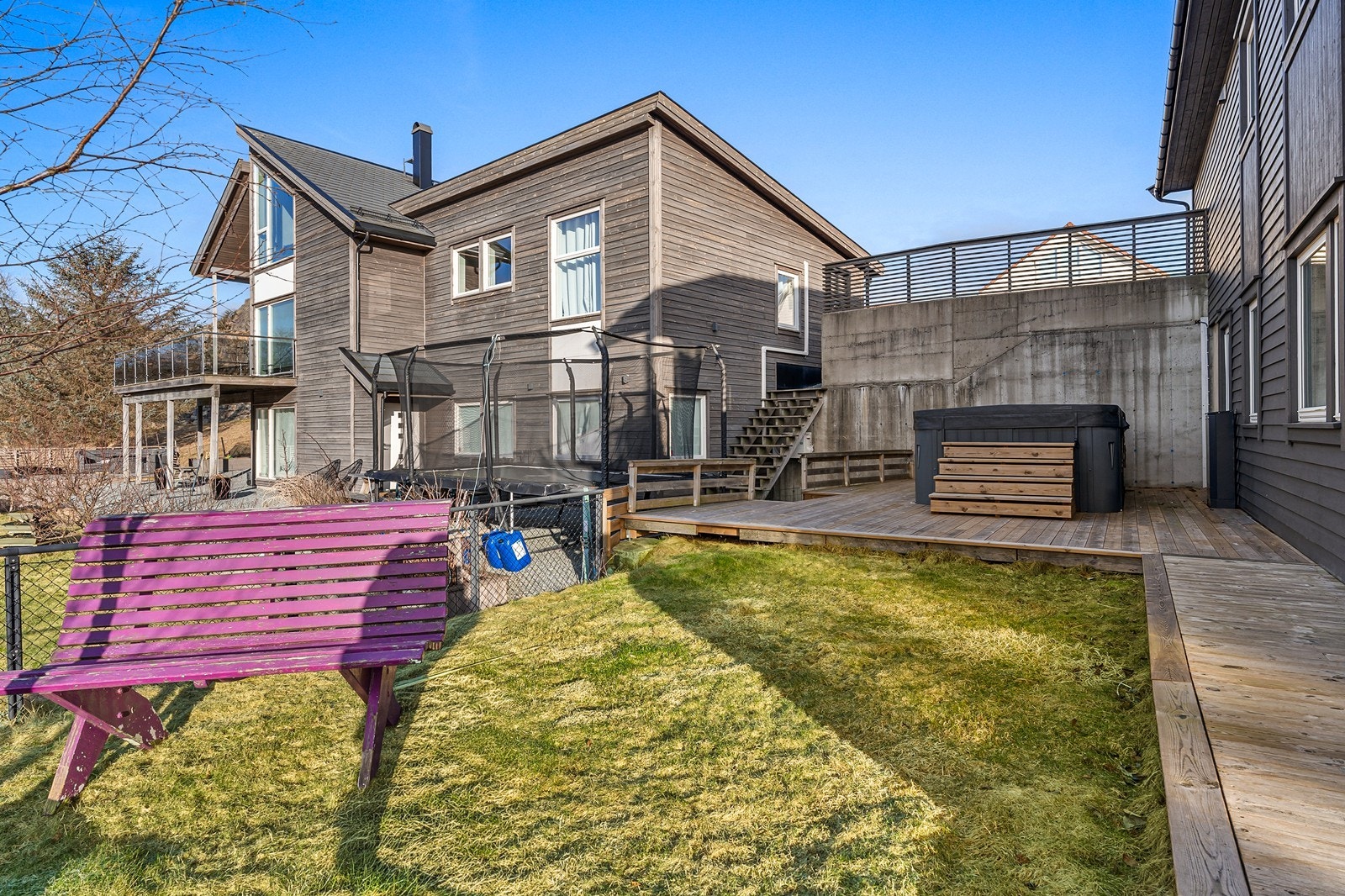 Eiendommen er pent opparbeidet med asfaltert areal til parkering, betongmurer mellom nivåene, flere treplattinger, plenareal og støttemur i naturstein i front. Galleribilde