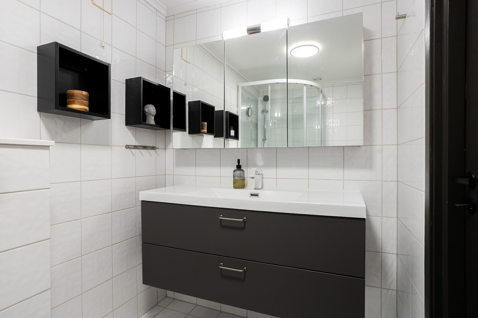 Innredningen består av nedfelt servant, veggmontert toalett og dusjkabinett. Det er for øvrig mekanisk avtrekk med tilluft under dør. Galleribilde