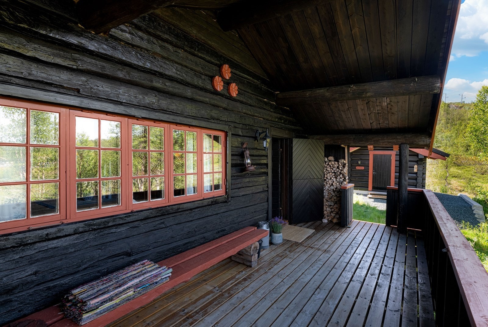 På fremsiden av hytta, ved inngangspartiet, er det en overbygget veranda med tett rekkverk og fint utsyn mot nærområdet. Verandaen er romslig, og har i dag en hyggelig sittebenk. Galleribilde